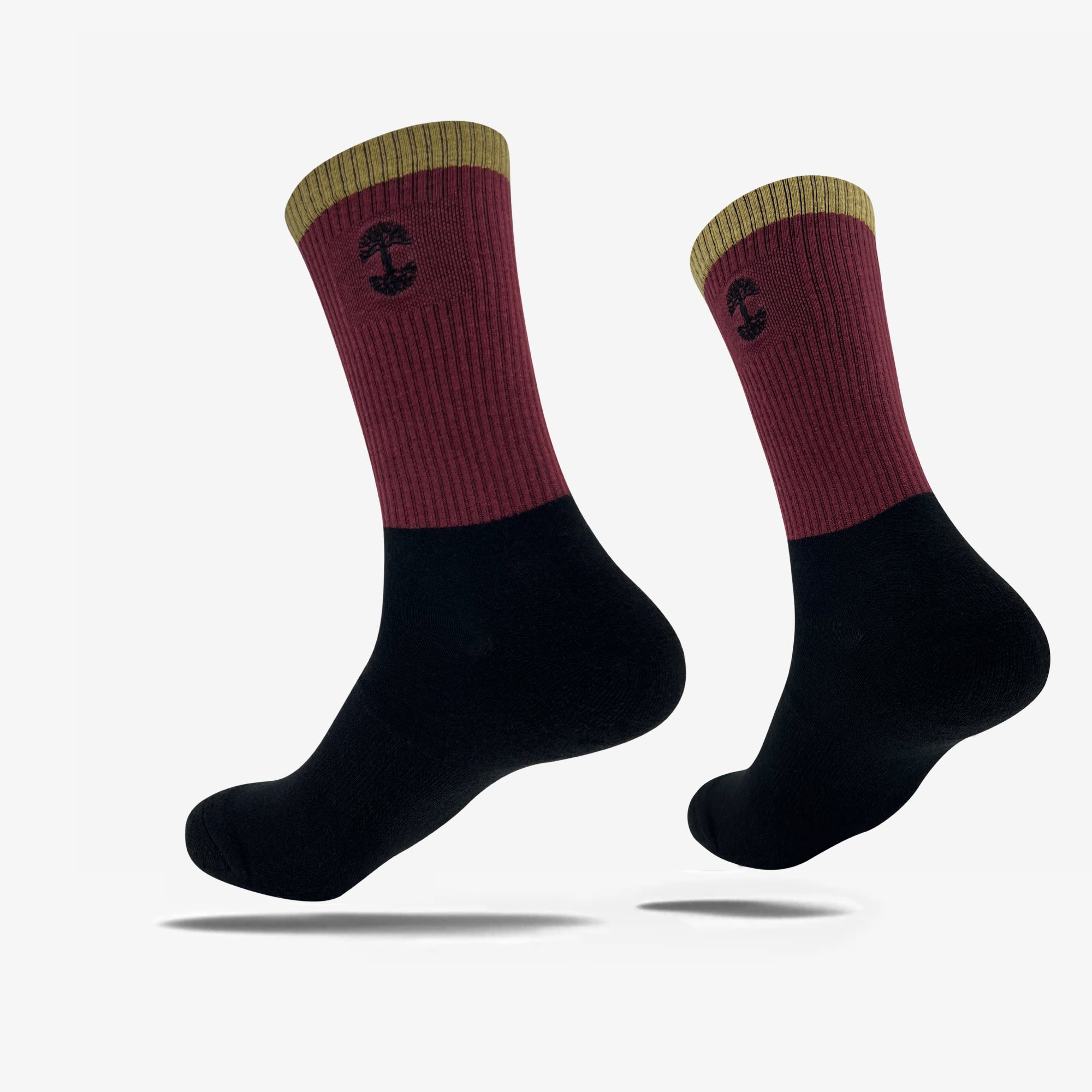 A pair of Oaklandish Colorblock socks features a two-tone design: the top half is burgundy with a yellow cuff and a small black mushroom emblem, and the bottom half is black. The socks are depicted against a plain white background, showing both side and bottom views.
