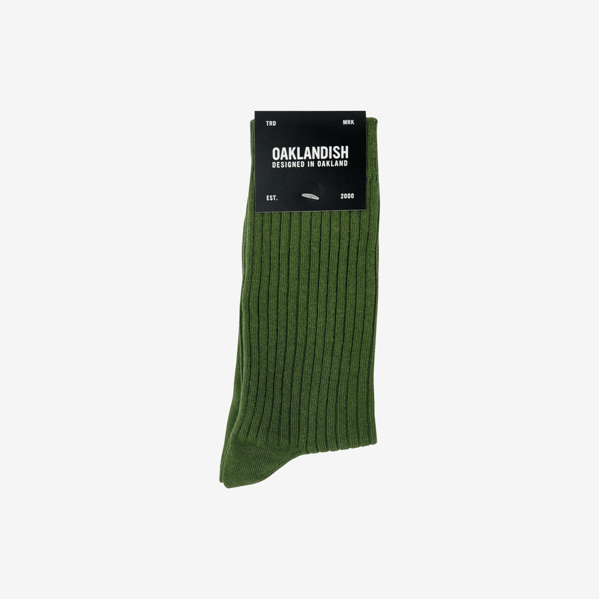 The Grip Crew Socks are shown in green with a ribbed texture. Packaged with a black label stating "OAKLANDISH Designed in Oakland" along with other text, these one-size-fits-most socks are neatly folded. The label is placed at the top against a plain white background.
