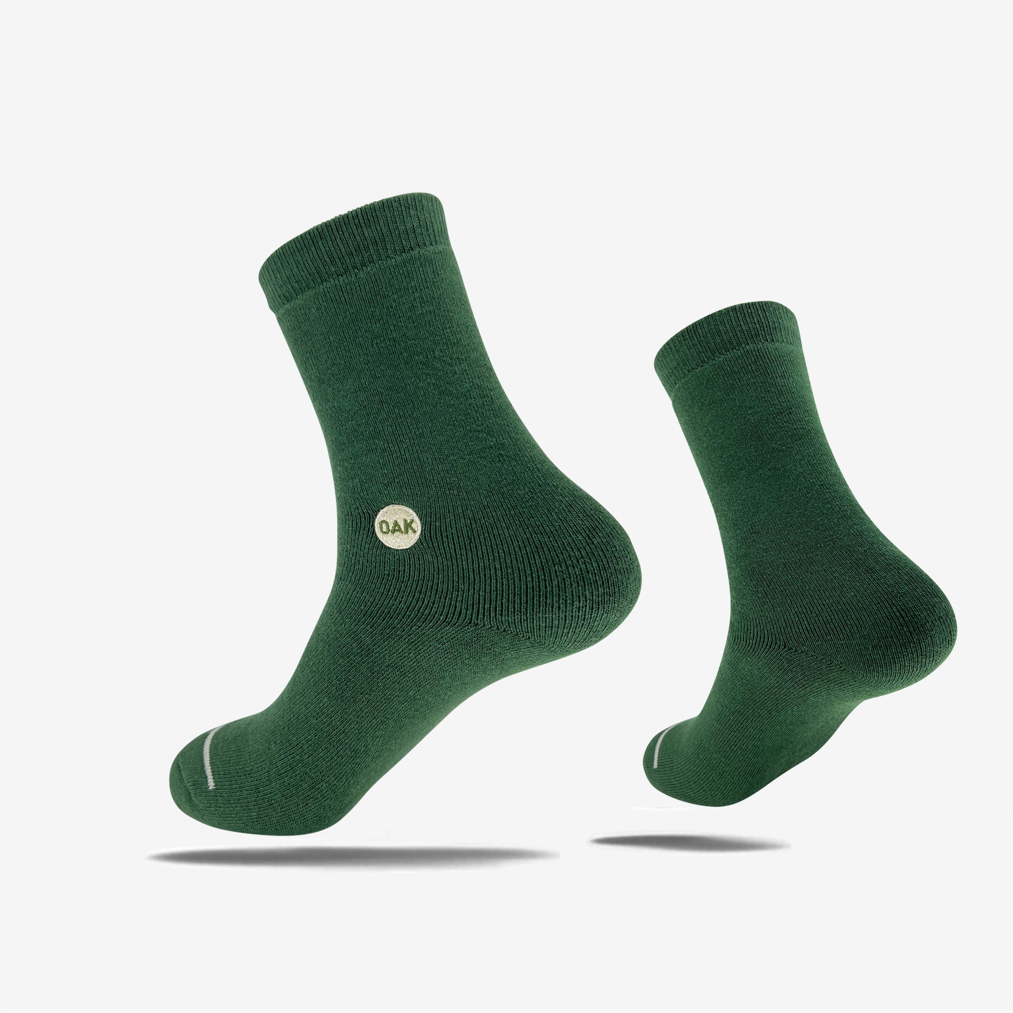 A pair of green Plush Oak Socks from Oaklandish is displayed against a plain white background. Crafted from soft cotton, these socks feature a ribbed cuff and a small circular "OAK" logo on the side. Artfully arranged, one sock presents a side view while the other is slightly elevated, promising happy feet.