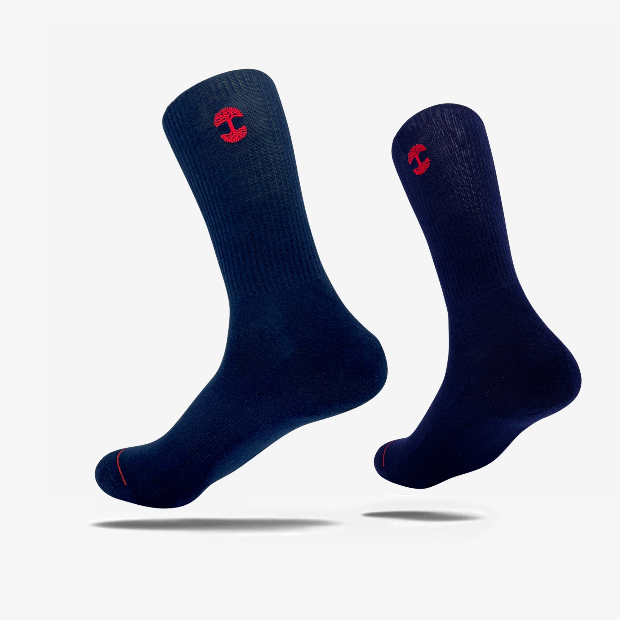 An image of the Embroidered Logo Sock by Oaklandish features two dark blue crew socks, each adorned with a red embroidered Oaklandish logo near the top. The socks are positioned upright with toes slightly pointed downward, creating a floating appearance against a white background. The adult-sized socks also have ribbed cuffs and a red accent line near the toes.