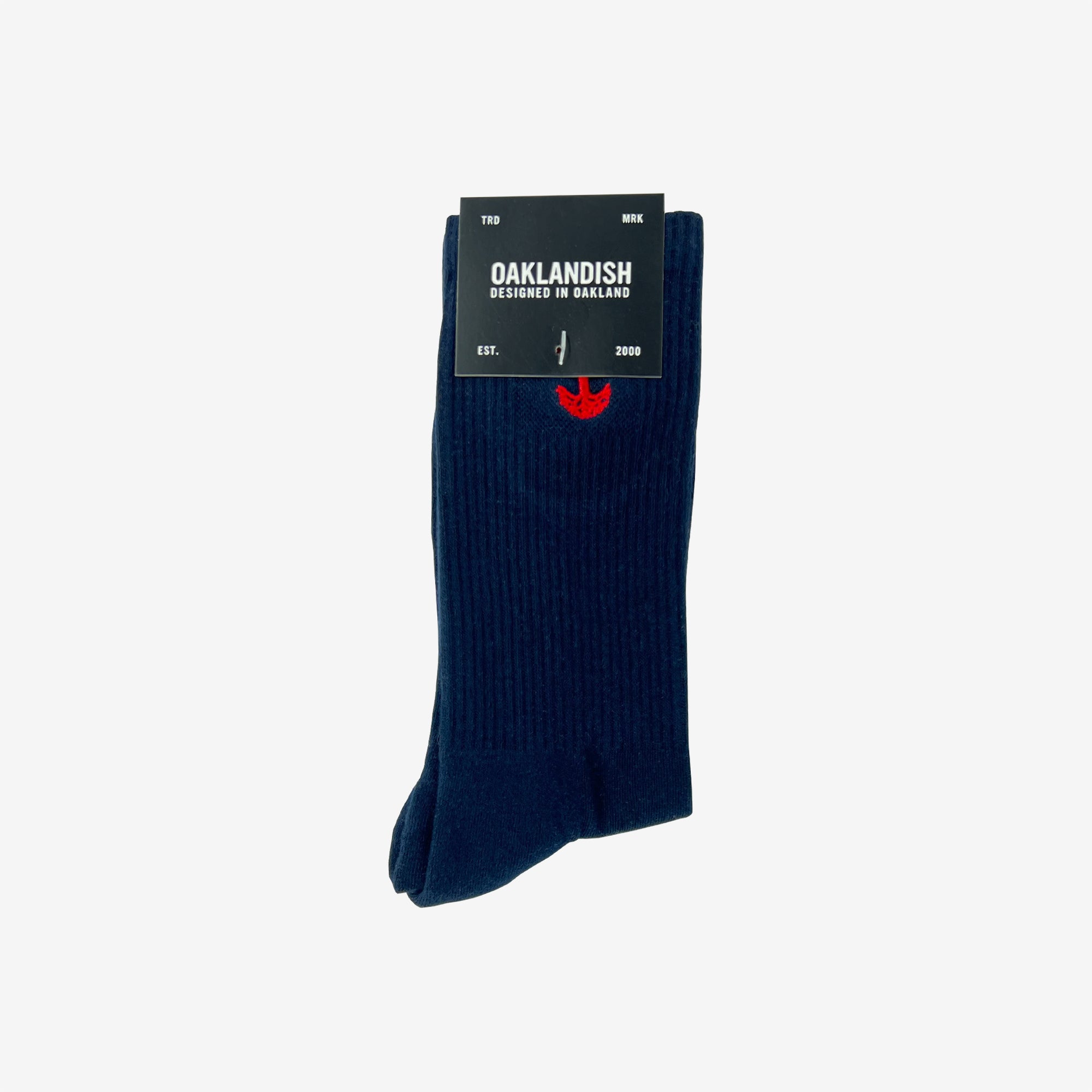 A pair of dark blue Embroidered Logo Socks is neatly folded, secured with a black label that reads, "OAKLANDISH, Designed in Oakland" with "EST. 2000" below. The adult-sized socks feature a subtle red embroidered Oaklandish logo near the top and have a ribbed texture.
