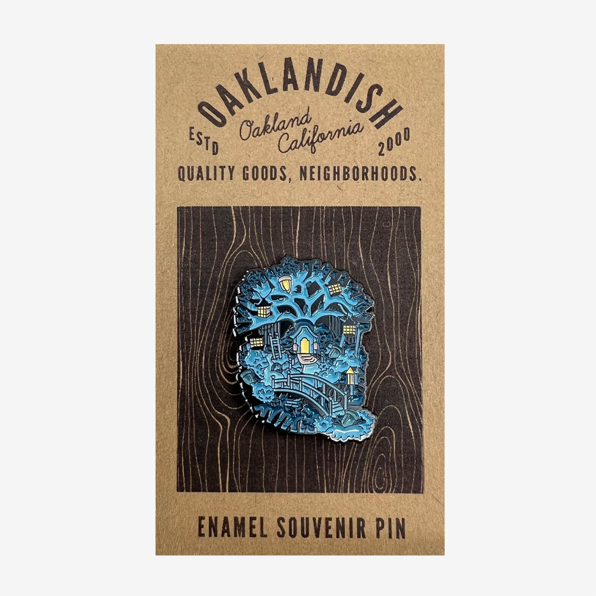 The Enamel Pin - Treehouse from Oaklandish showcases a vibrant nightscape of Oakland, California, with city landmarks in blue and yellow hues. It is mounted on a brown card that features the text "OAKLANDISH," "Est'd Oakland, California 2000," and "Quality Goods, Neighborhoods," with "Enamel Souvenir Pin" at the bottom. This pin is perfect for fans of stylish accessories.