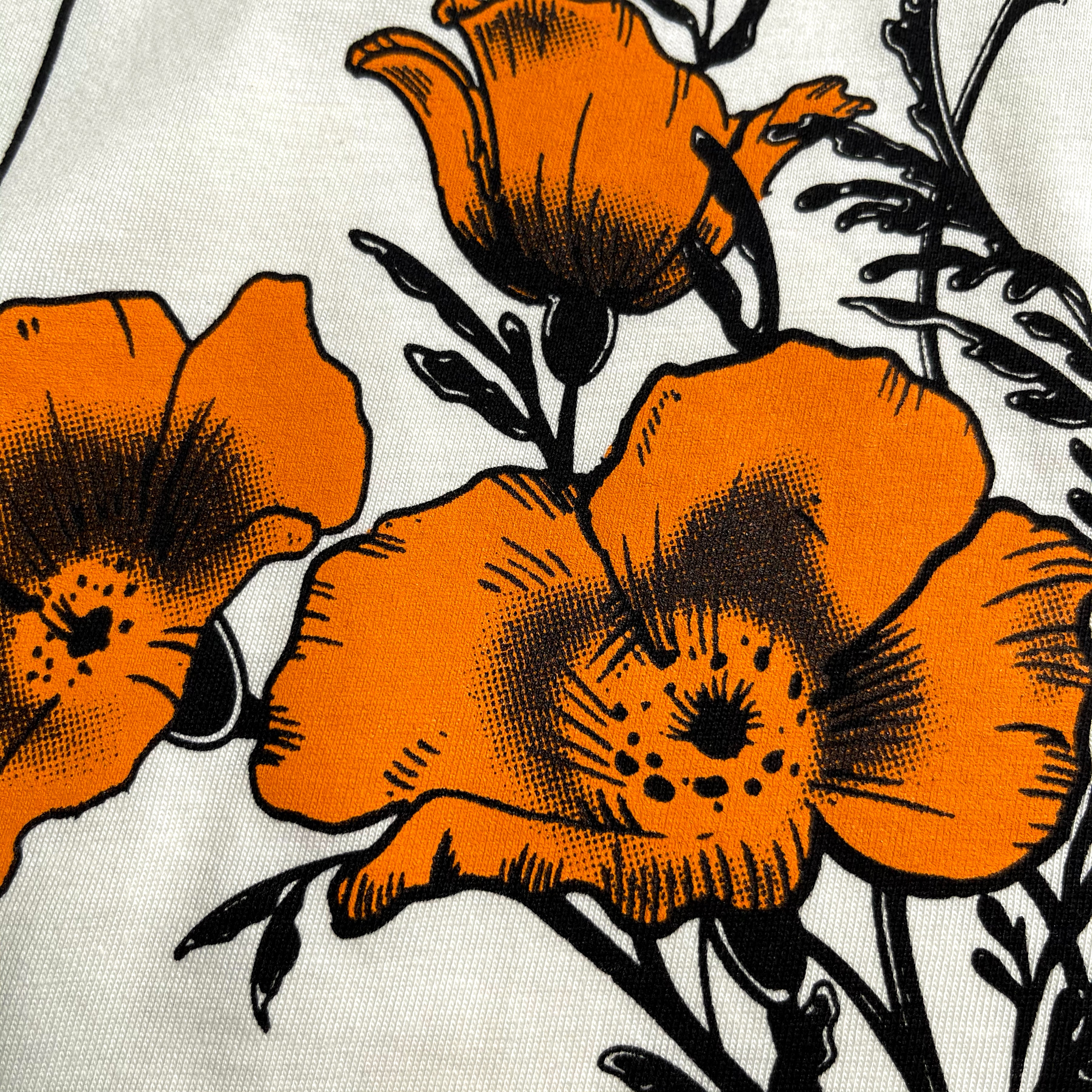 A close-up illustration of vibrant orange poppy flowers with black outlines and detailed shading on a white background. The blooms are fully open, showcasing delicate petals and intricate centers, with black stems and leaves adding contrast to the overall design on this 100% cotton Women's Blossom Tee by Oaklandish.