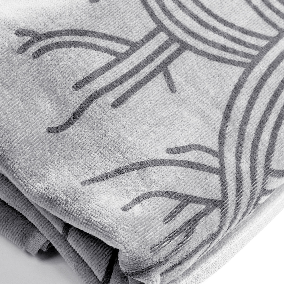 A close-up of the oversized Classic Logo Beach Towel by Oaklandish, folded to reveal its abstract, elegant darker gray tree design. Made from 100% ringspun cotton, the fabric appears super soft and plush with visible textures and fibers. The towel's folds highlight the intricate pattern and high-quality material.