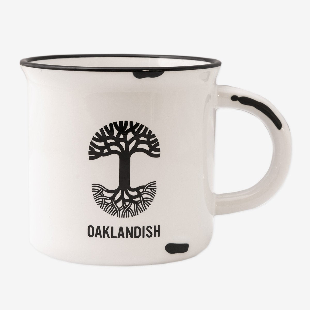 The 15 oz Ventura Mug by Oaklandish is a white ceramic stoneware mug featuring a black rim at the top and a black handle. The mug displays an artistic black tree design with the word "OAKLANDISH" below it, celebrating Oakland city pride. There is a small irregular black spot near the base and handle.