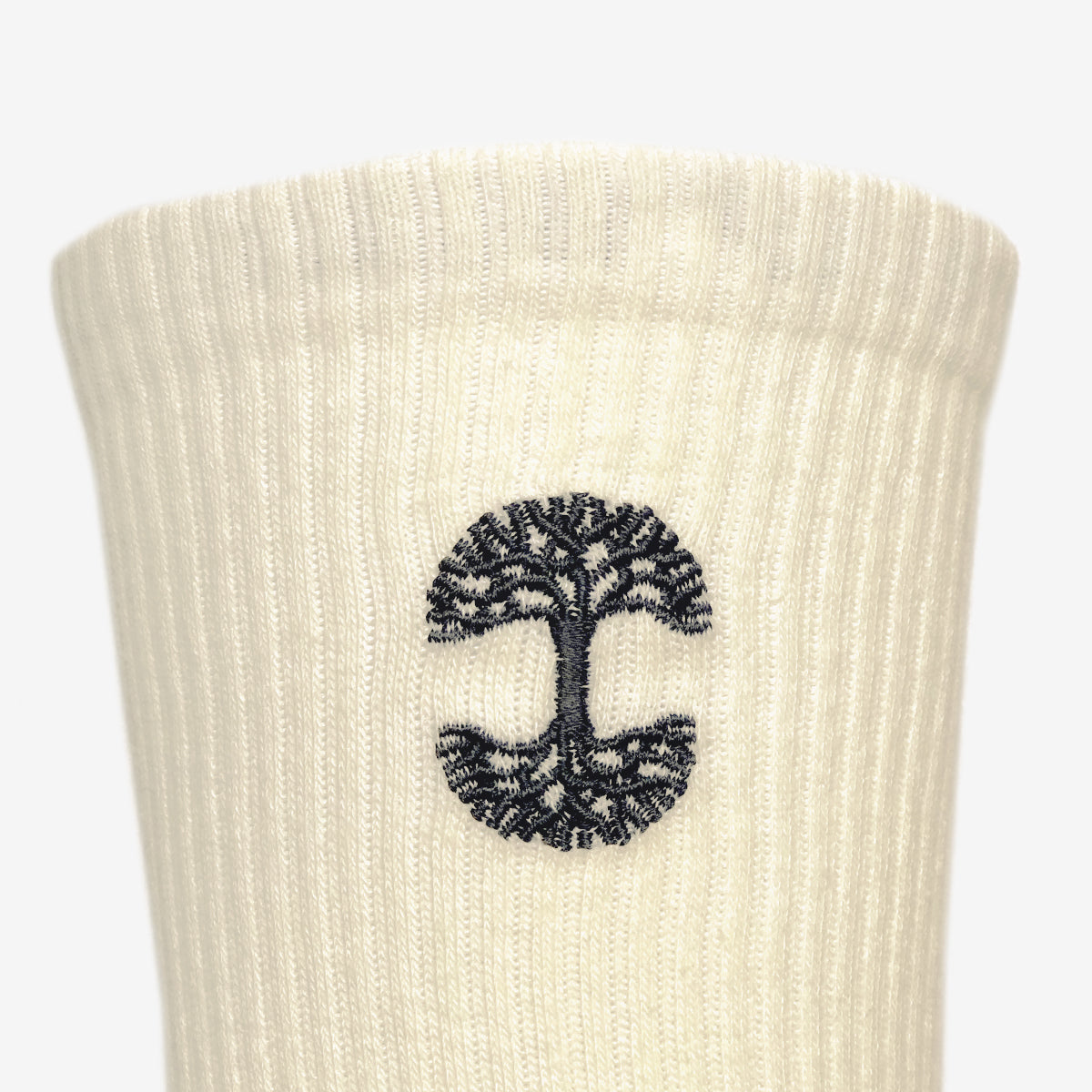 Close-up of the white ribbed fabric from the Oaklandish Embroidered Logo Socks, featuring a black tree of life design. The symmetrically spread roots and branches are enclosed within a circular border, centered on the socks, showcasing the iconic Oaklandish style.