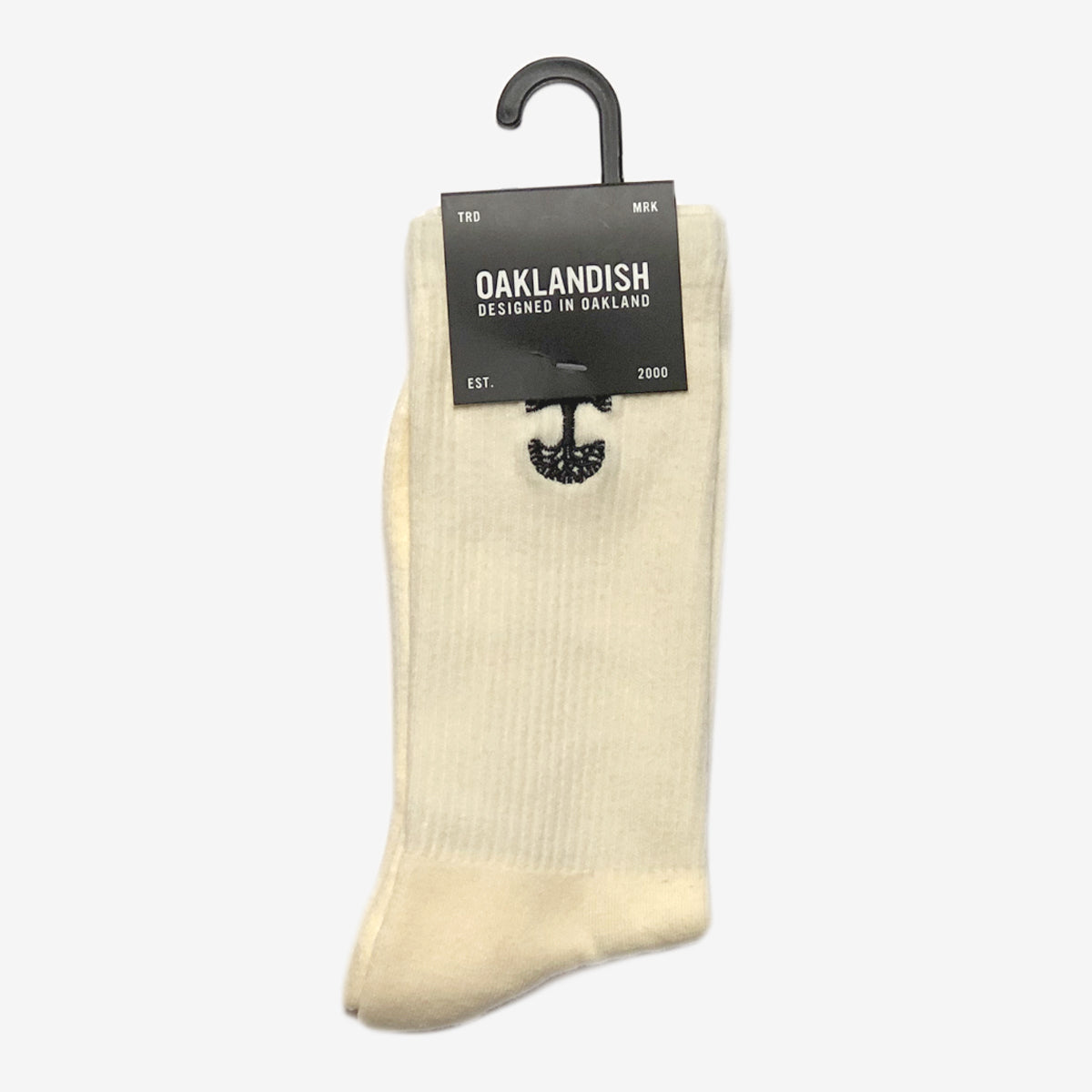 A pair of yellow cotton Embroidered Logo Socks is displayed against a plain background. Neatly folded and held together by a black hanger, they feature an embroidered logo. Attached to the hanger is a dark gray label reading "Oaklandish, Designed in Oakland," accompanied by an image of an oak tree. The label also notes "TRD MRK" and "EST. 2000".