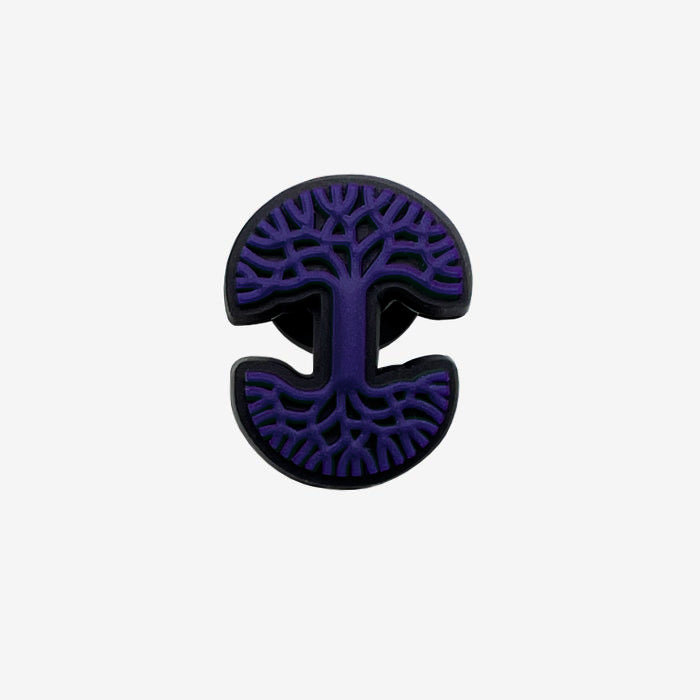 Introducing the Oaklandish Logo Charm by Oaklandish: This distinctive accessory showcases a vibrant purple tree design set against a dark backdrop. The intricate branches extend to the edges, creating a symmetrical pattern that resembles both a tree and a stylized letter "I" at the center. This circular charm features slight cutouts at the top and bottom, making it an ideal addition as a shoe adornment.