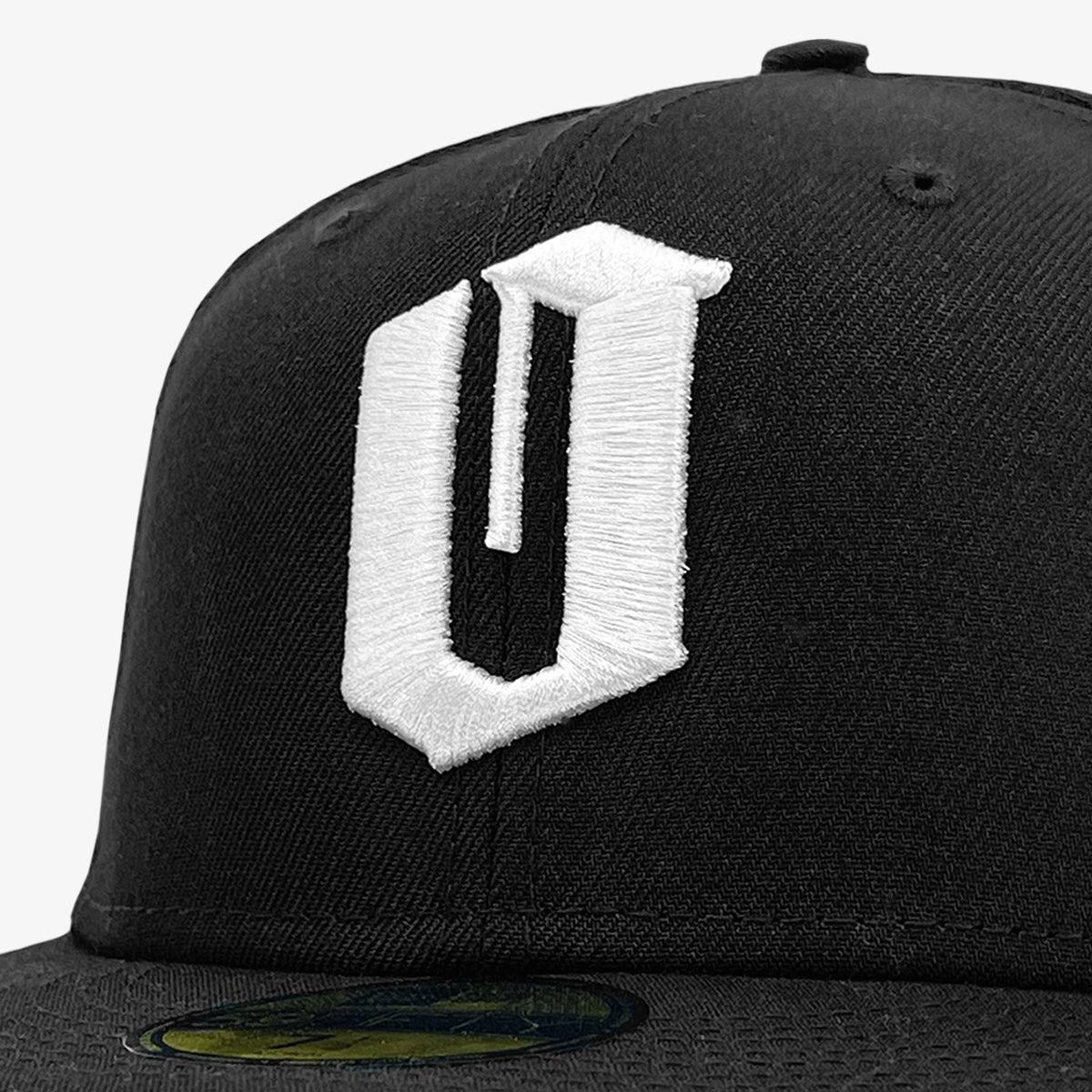 Close-up of the New Era Official 59FIFTY Fitted Cap by Oaklandish, showcasing a white embroidered letter "U" on the front. The visor is partially visible with a holographic sticker on it, set against a plain white background.