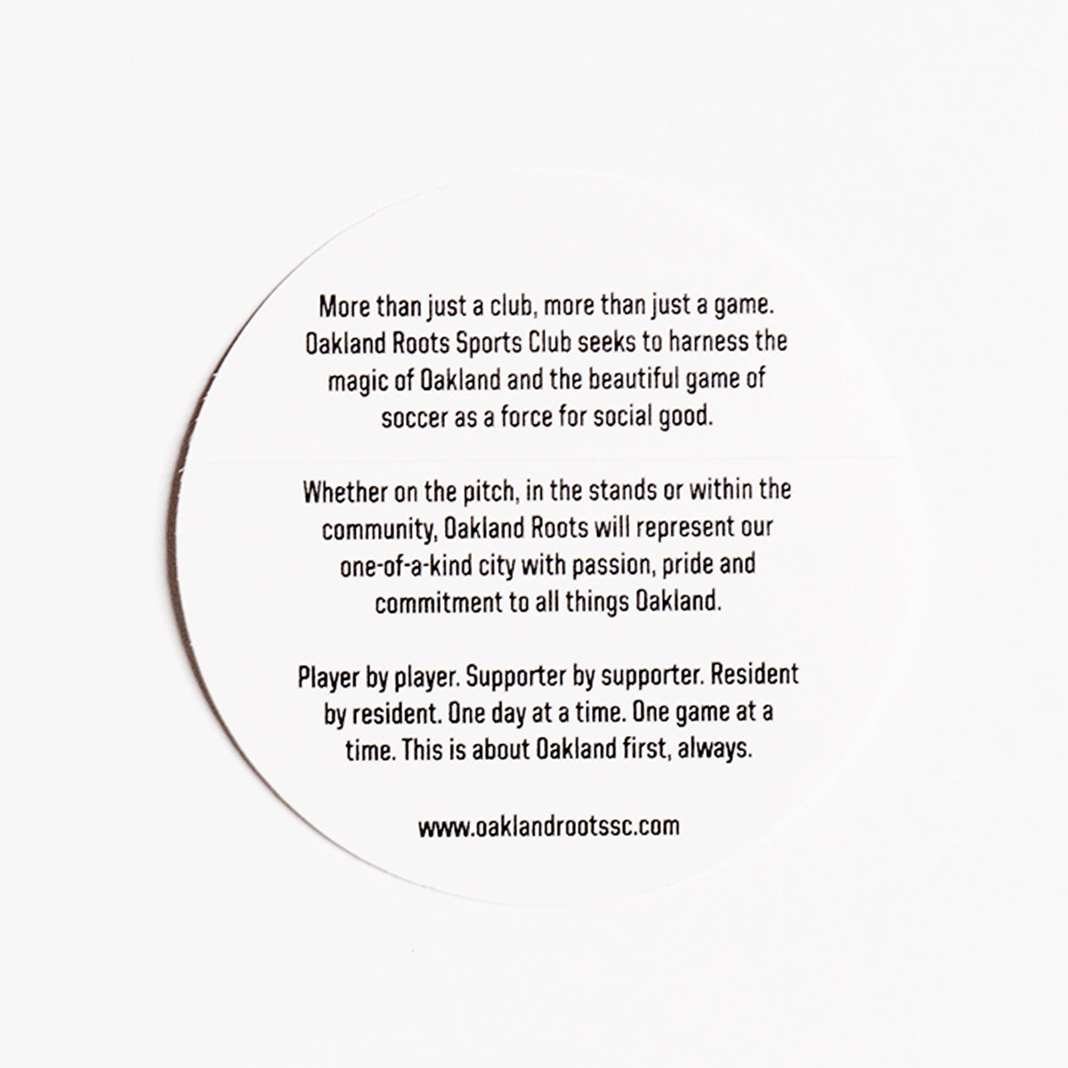 A round, white Oakland Roots SC Logo Sticker from the Oakland Roots SC brand, featuring black text that promotes the club's mission of using soccer for social good. The text emphasizes representing Oakland with passion and pride, highlighting their commitment to community and unity through the sport. The design feels akin to an Oaklandish sticker, showcasing local love. For more details, visit www.oaklandrootssc.com.