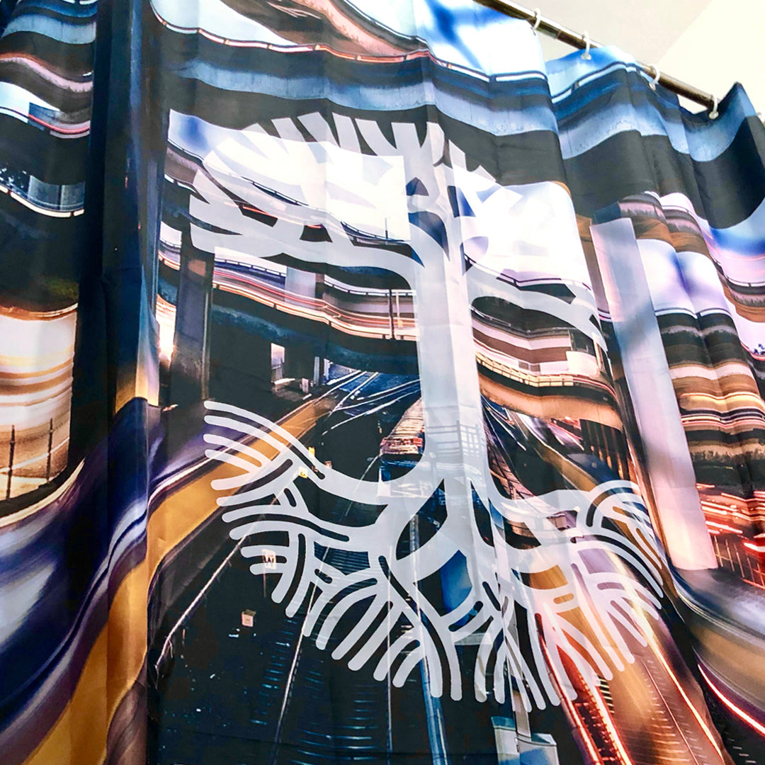 The Overpass Shower Curtain 72 X 72 by Oaklandish features an abstract design of a white tree, with roots depicted at the bottom. The background showcases blurred, colorful lights resembling a long-exposure photograph of a highway or cityscape, creating a dynamic visual effect. Perfect for adding style to your bathroom, this polyester curtain is hung on a metal rod.