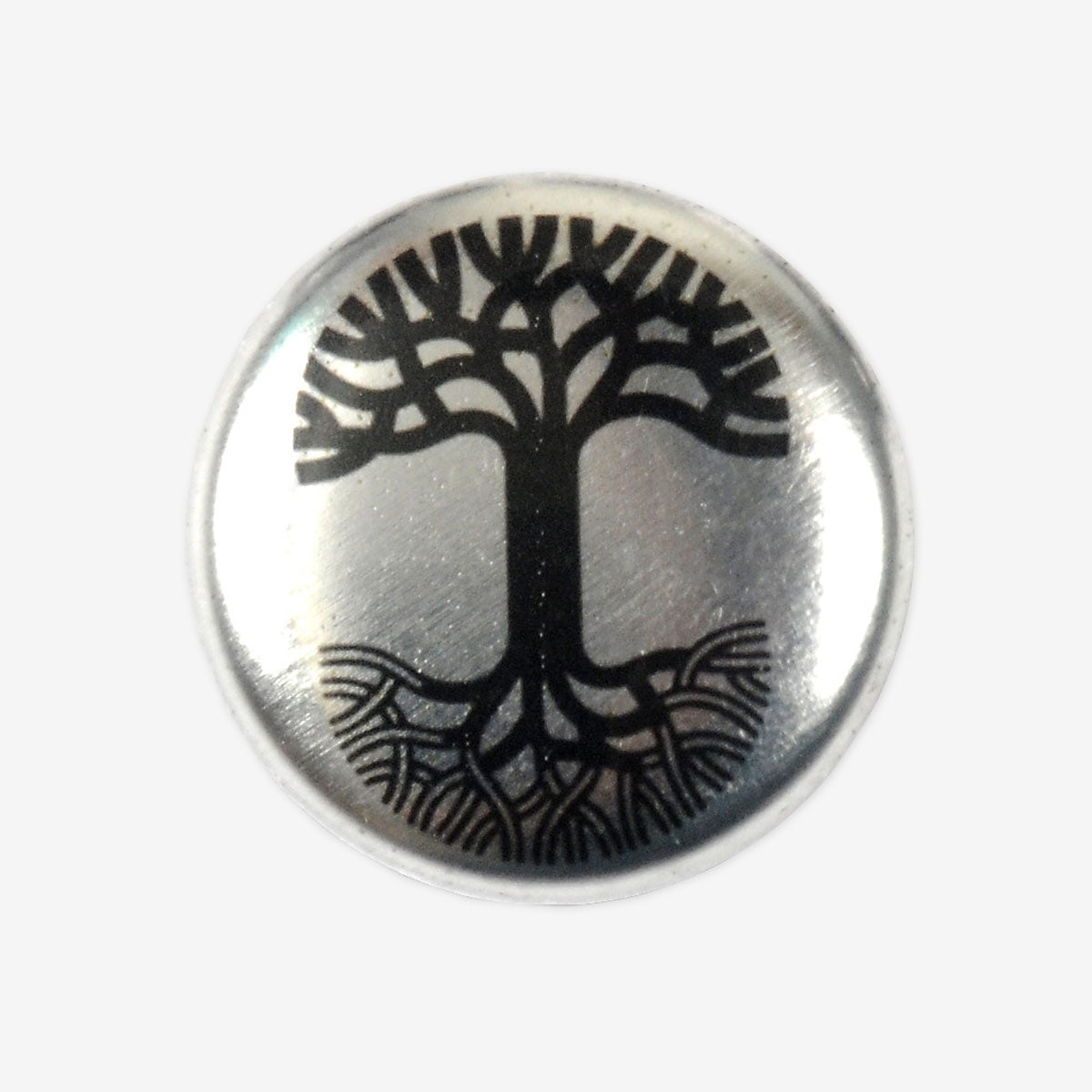 The Oaklandish Pin by Oaklandish is a round pin with a silver metallic background that displays a black tree design. The tree features stylized branches and roots in a symmetrical pattern, creating a balanced and intricate visual effect, complemented by the background's slight reflective sheen.