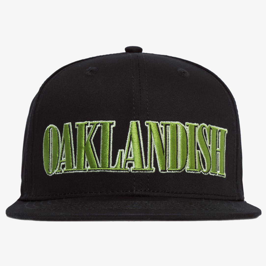 The Greenback Snapback by Oaklandish is a black cap with the word "OAKLANDISH" embroidered in large, green, capital letters on the front. This headwear features a flat brim and six ventilation eyelets, with two visible in this view.