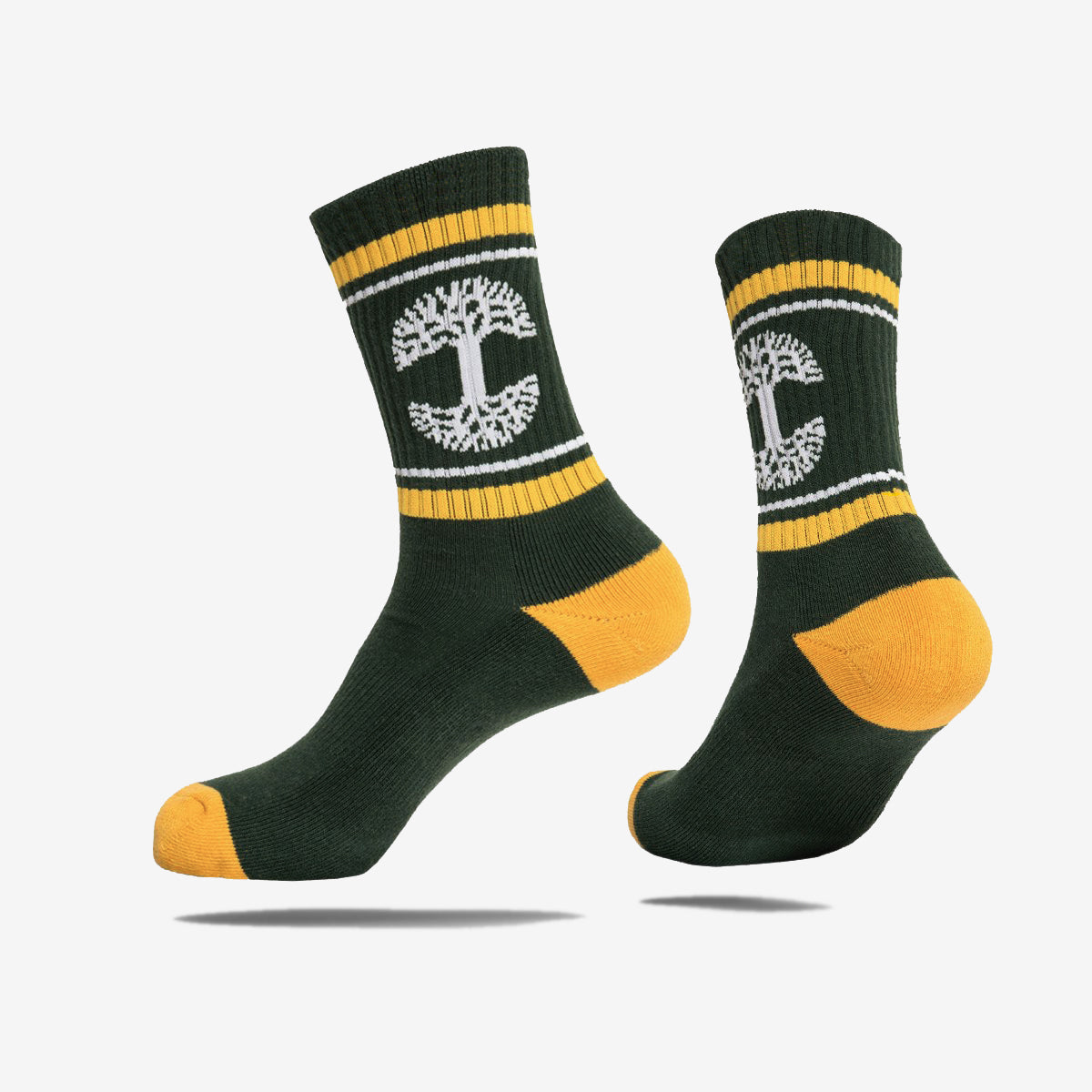 Introducing the OAK Knit Crew Socks by Oaklandish. These socks come in a forest green hue with striking yellow accents on the toe, heel, and top cuff. Adorned with white stripes around the cuffs and featuring a distinctive white tree emblem on the sides, they are crafted from a comfortable blend of cotton, polyester, and spandex. Displayed against a plain white background, one sock is angled to prominently showcase the iconic tree design.