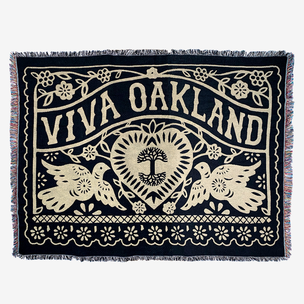 Introducing the Viva Oakland Throw from Oaklandish: This woven tapestry, crafted from recycled fibers, features "Viva Oakland" in large, bold letters at the top. A central heart adorned with a tree design is surrounded by floral and intricate patterns. Two birds symmetrically face the heart, adding to its charm. The throw is finished with a decorative cotton fringe along the edges for a unique touch.