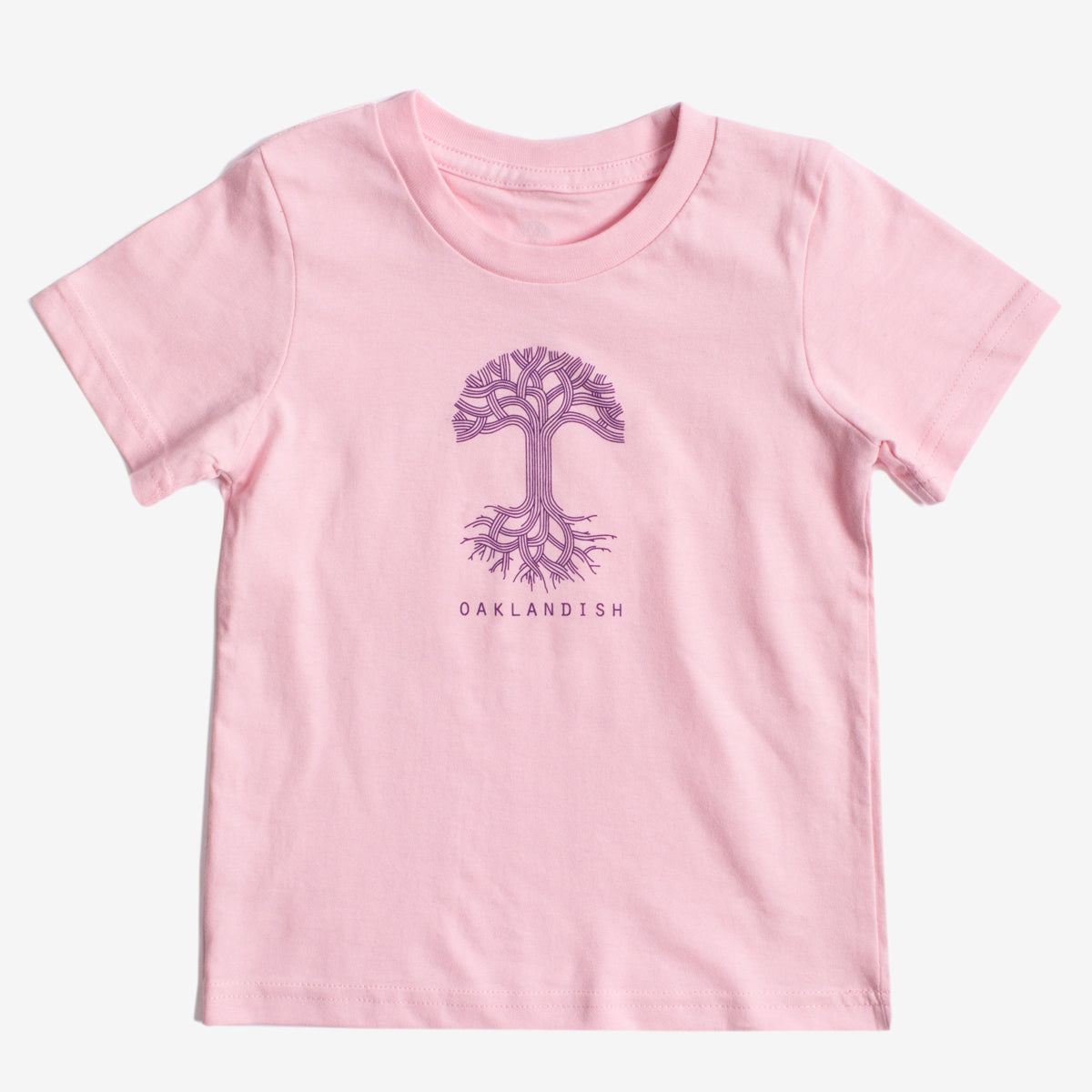 A light pink, 100% cotton Toddler Oaklandish Classic Logo Tee from Oaklandish featuring a purple tree graphic with intricate branches and roots in the center. Below the tree, "OAKLANDISH" is printed in a simple, all-caps font. The t-shirt is laid flat against a white background.