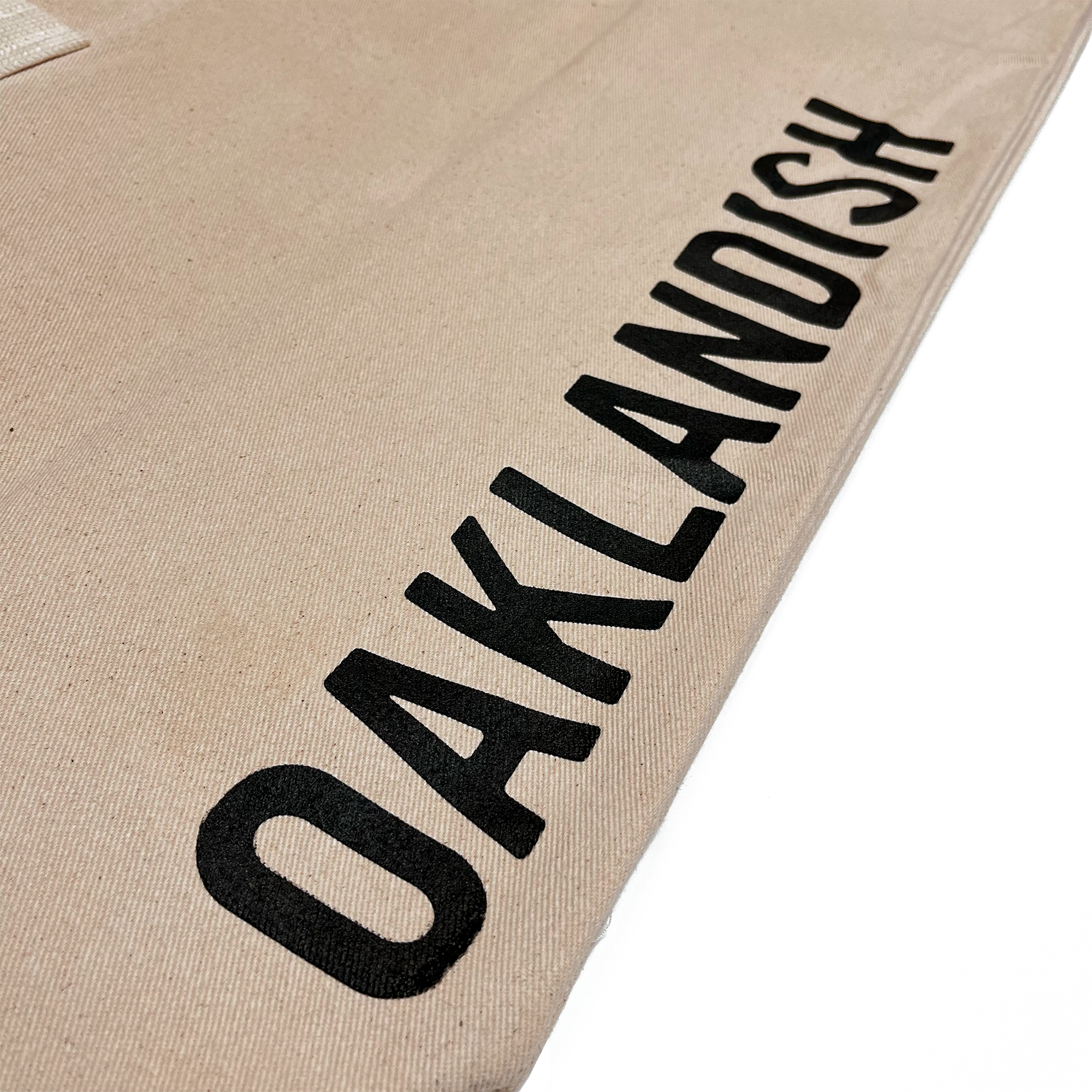 Close up of Oaklandish wordmark on brown natural denim extra large tote bag.
