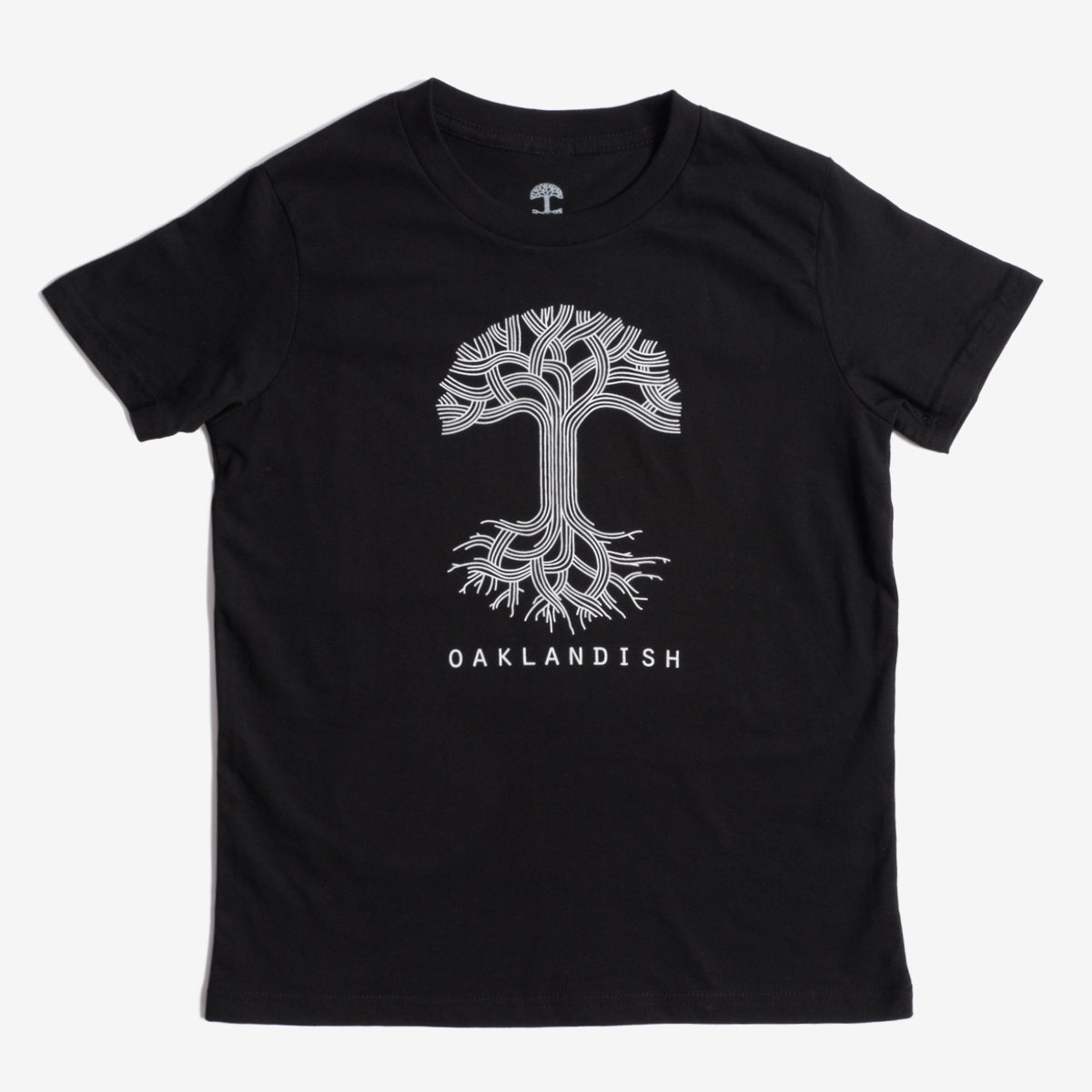 The image shows the Youth Oaklandish Classic Logo Tee by Oaklandish, a black tee made from 100% cotton. It features a white graphic of a tree with branches extending upward and roots spreading downward. Below the tree graphic, "OAKLANDISH" is written in white capital letters. The kids' t-shirt is laid flat against a white background.
