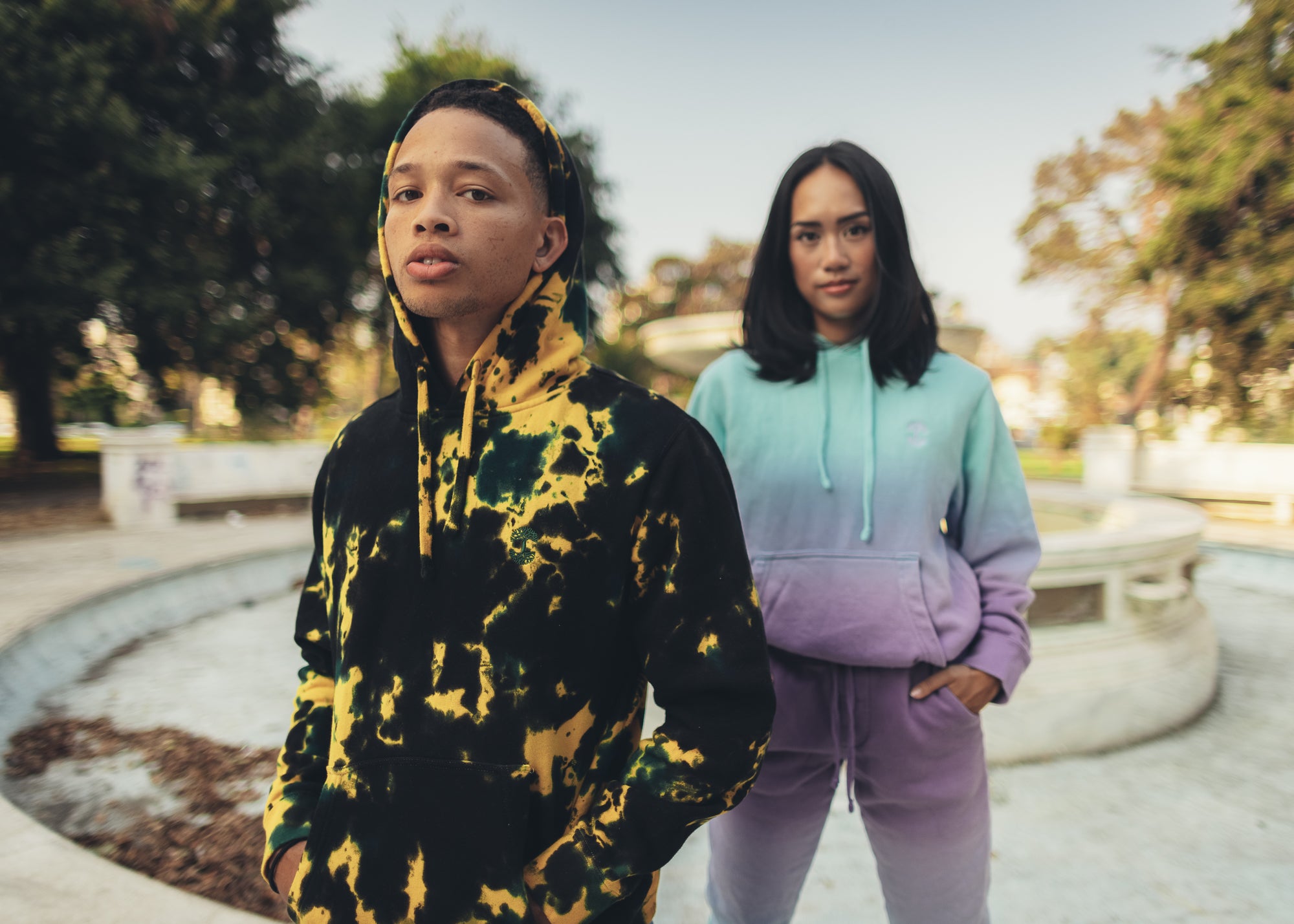 Guy in green/yellow/black tie dyed hoodie and girl in ombre hoodie and joggers.