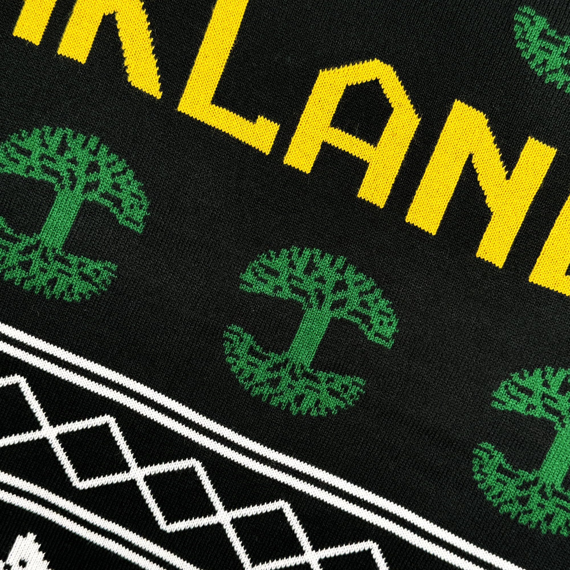 A close-up of the Oaklandish 2024 Ugly Sweater reveals a black knit design featuring "OAKLAND" in bold yellow letters. Beneath, it boasts stylized green tree graphics and a striking geometric pattern of white zigzags and diamonds, making it an excellent addition to your outerwear collection.