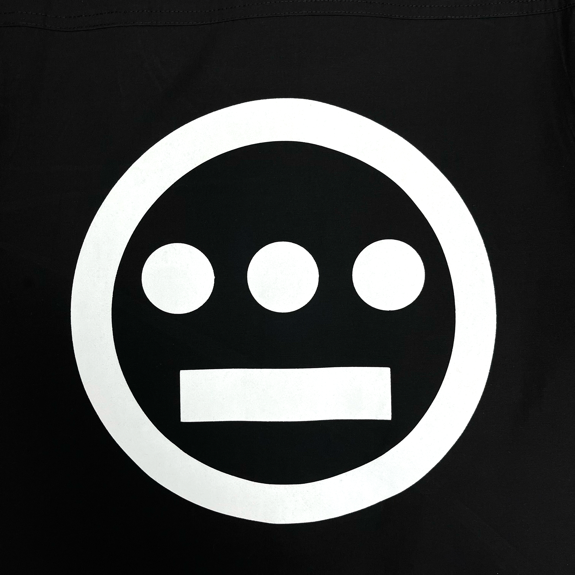 The Hieroglyphics Premium Coaches Jacket from the brand Hieroglyphics features a black background highlighting a white symbol that resembles the Hieroglyphics logo. The design consists of a large circle with three evenly spaced smaller solid circles arranged horizontally at its center, accompanied by a solid horizontal bar below them. This creates a clean and geometric appearance.