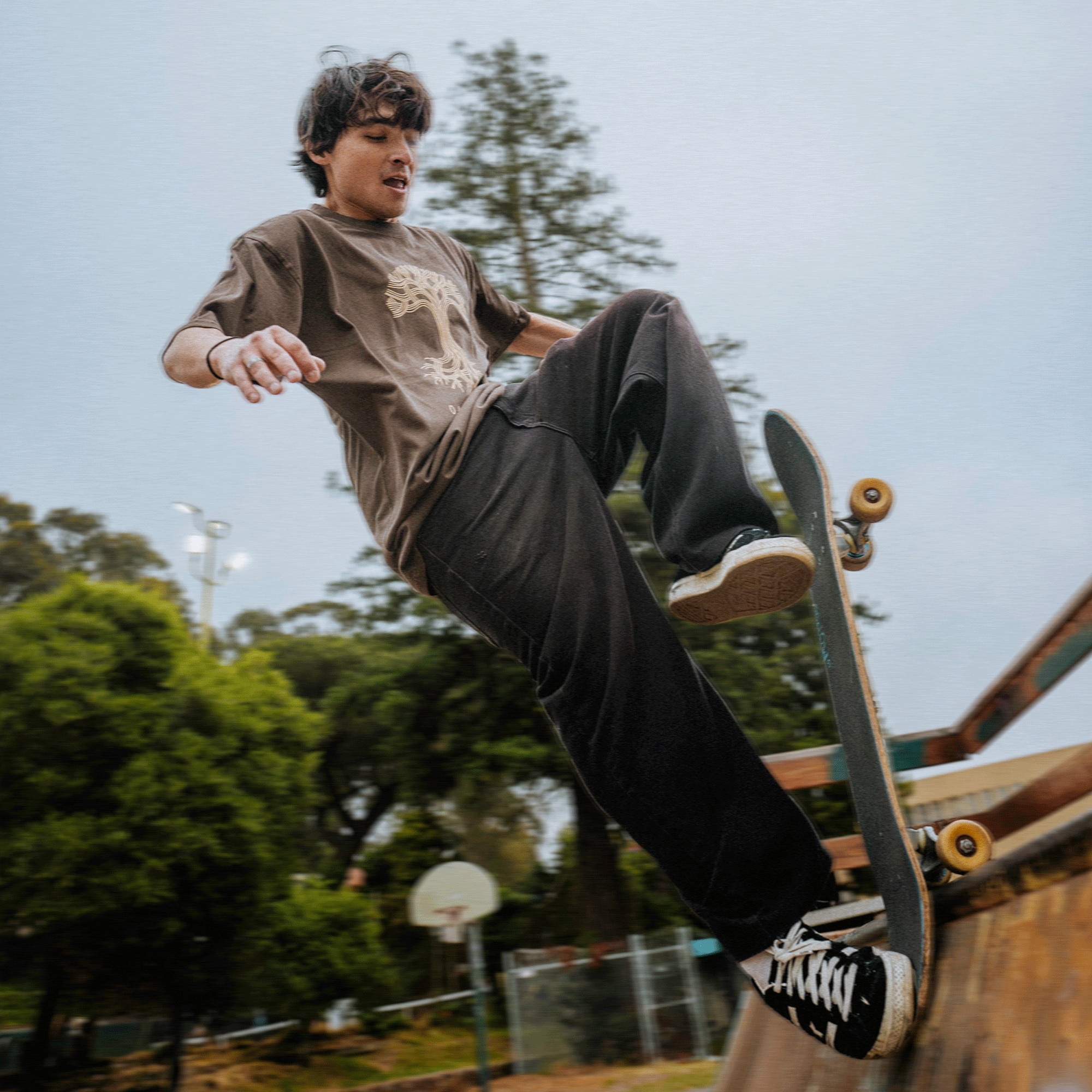 Model skateboarding while wearing Oaklandish classic heavy logo tee faded brown.