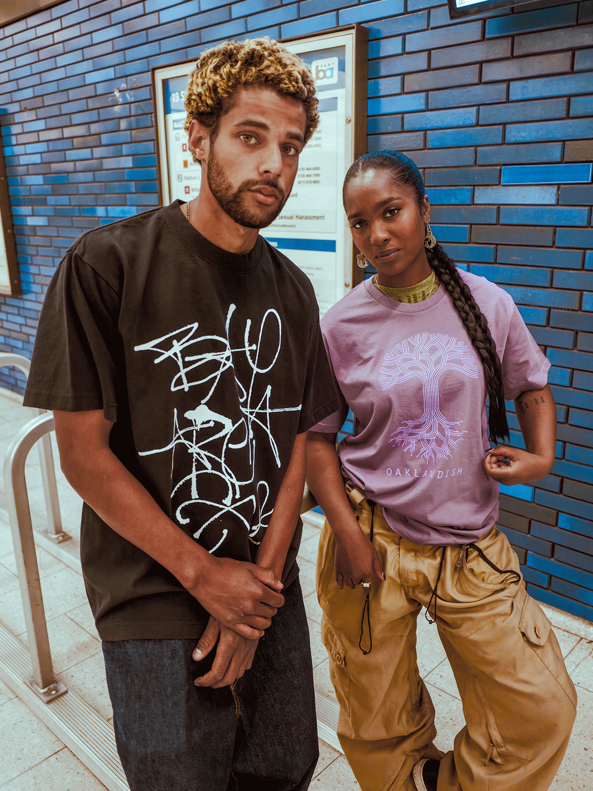 Two people standing against a blue brick wall with in BART station.