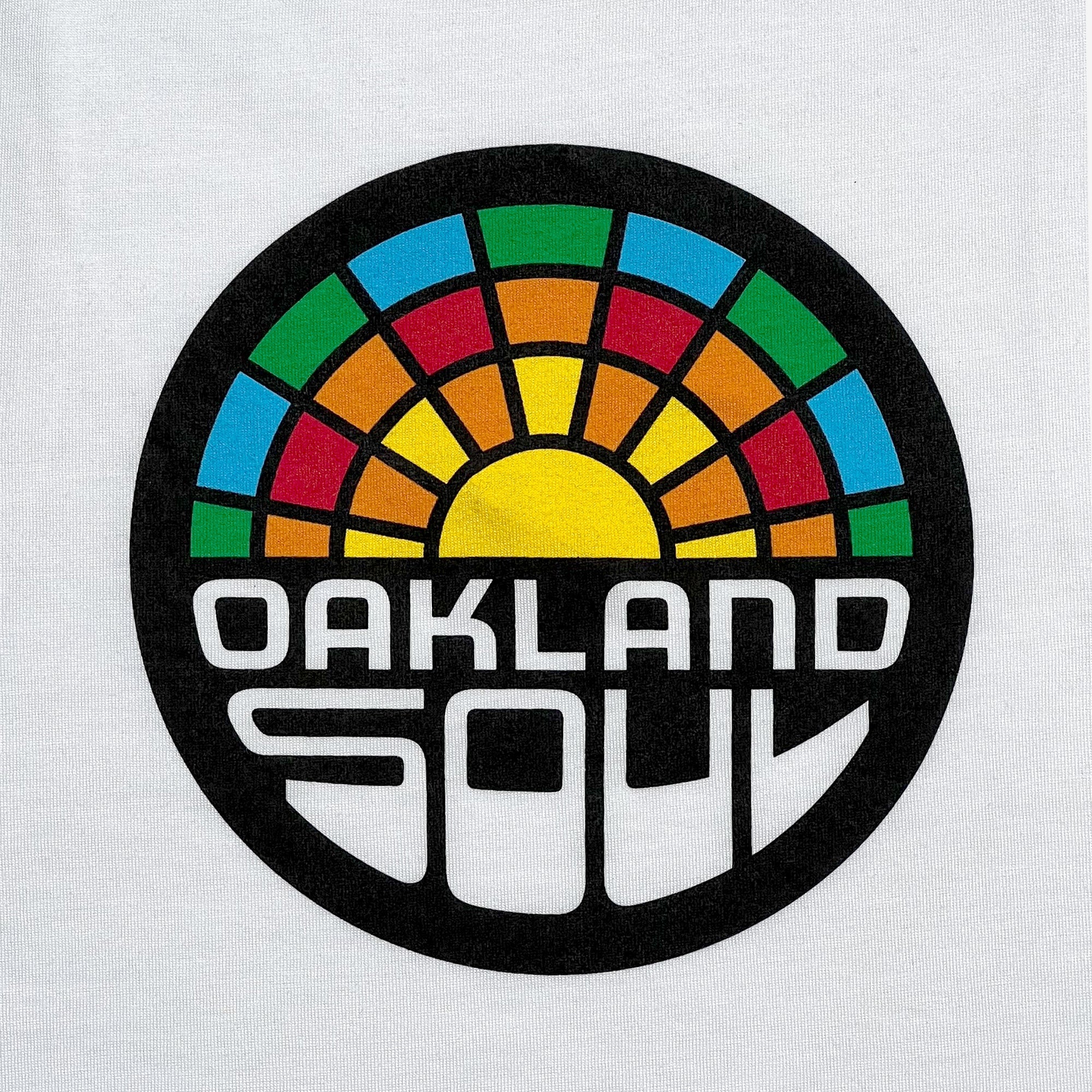 The Women's Oakland Soul Logo Tank by Oakland Roots SC showcases a circular logo with a vibrant mosaic-like design. Colorful segments in green, blue, red, and yellow form the pattern above a sun icon. The bold, modern text "Oakland Soul" is displayed below the design. Perfect for adding flair to any outfit, this eye-catching logo stands out against the white tank top background.