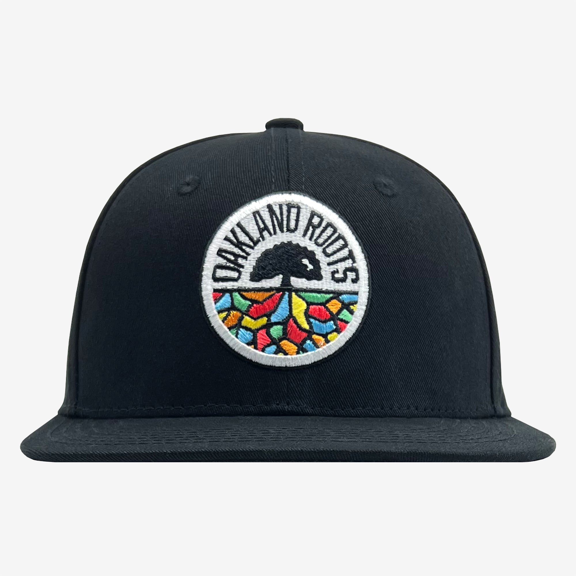 The Oakland Roots SC Structured Snapback, by Oakland Roots SC, is a black baseball cap with a flat brim that features a circular embroidered logo on the front. The logo displays the text "Oakland Roots" encircling a black tree. Beneath the tree, vibrant geometric shapes in red, yellow, and green create a mosaic-like effect. This cap is perfect for fans of this energetic sports club or anyone who appreciates Oaklandish style.