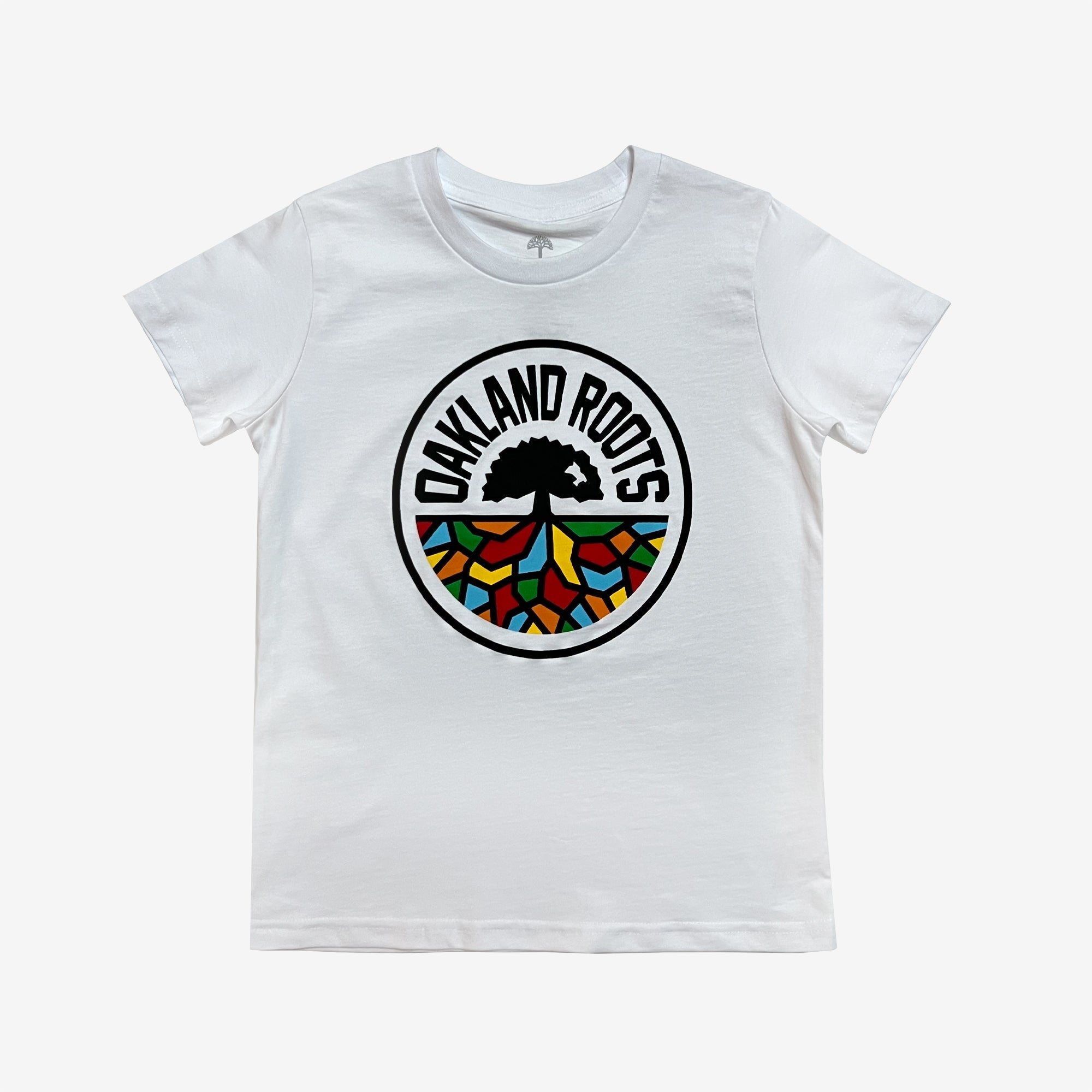 The Youth Oakland Roots SC Classic Tee by Oakland Roots SC is a white short-sleeve t-shirt featuring a colorful emblem in the center. The circular emblem includes a black silhouette of a tree with the words "Oakland Roots" curving around the top. The lower section of the emblem contains a mosaic of vibrant colors: red, yellow, green, and blue, reflecting their commitment to social good.