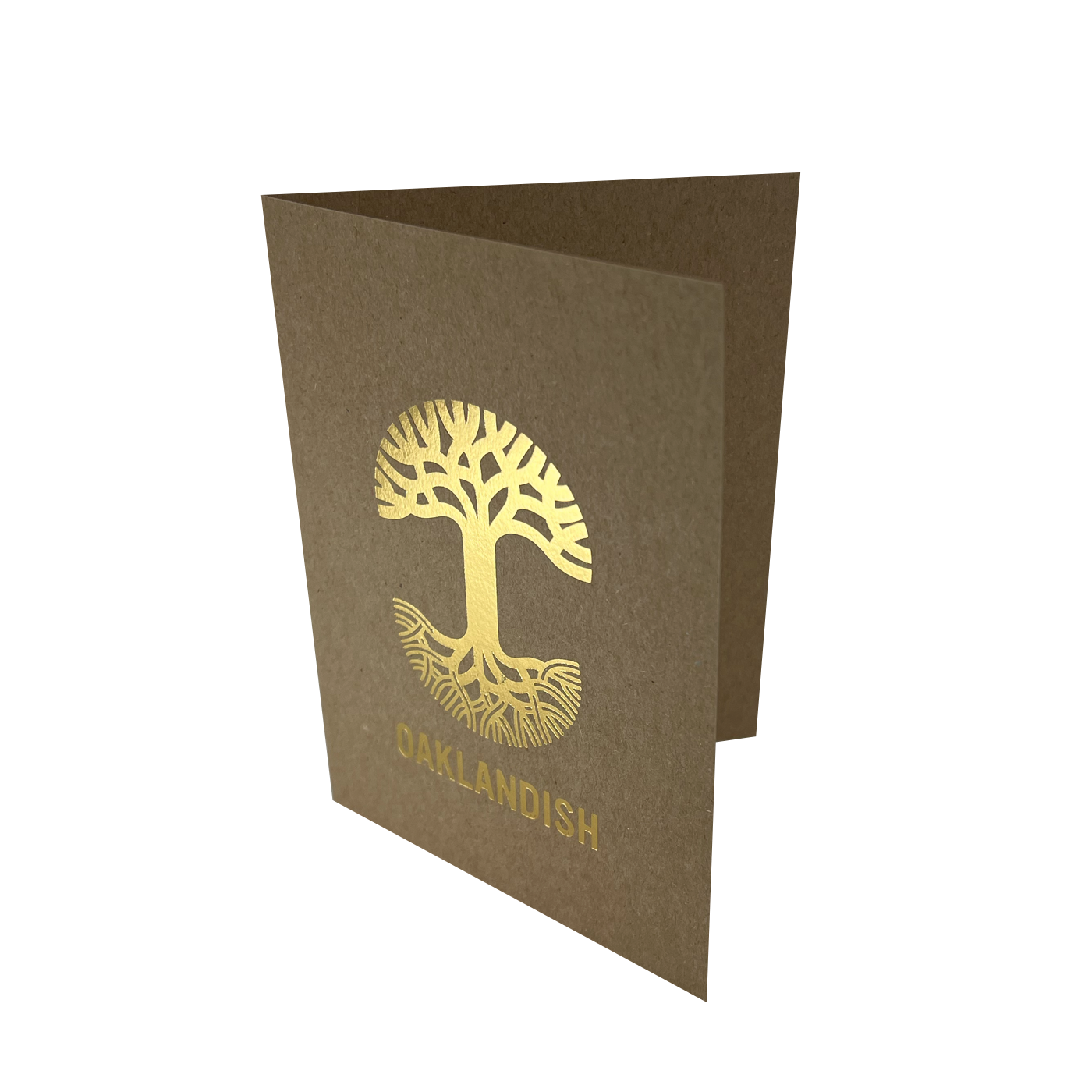 The Oaklandish New Logo Card by Never Elsewhere is a minimalist greeting card made of recycled brown kraft paper, shown partially open. The front showcases a gold tree with intricate roots and branches, printed using letterpress. Below the tree, "OAKLANDISH" is displayed in gold capital letters. The card rests on a white background.