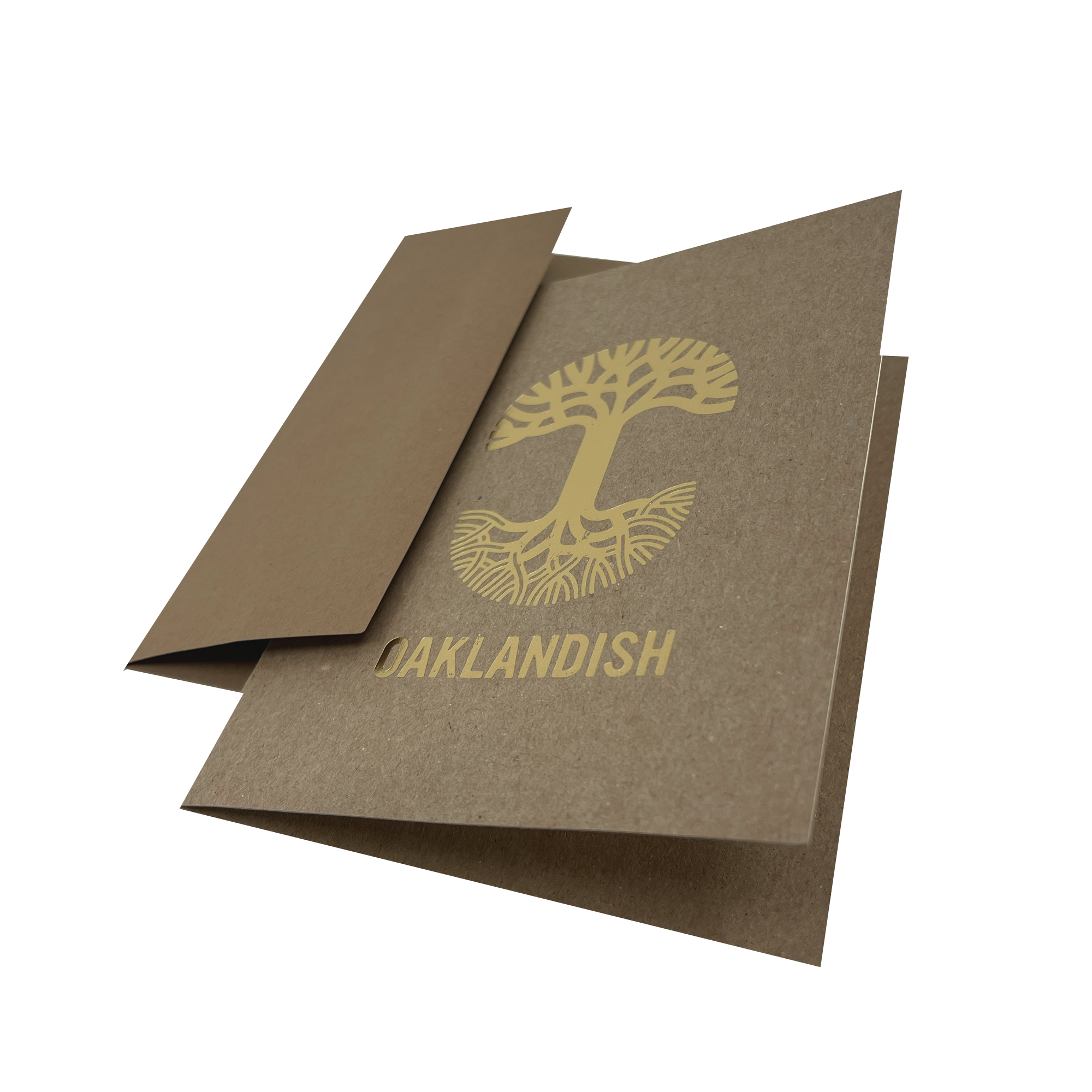 An "Oaklandish New Logo Card" by Never Elsewhere, crafted from recycled brown kraft paper, lies partially open on a white background. The card displays a stylized gold tree with exposed roots and the word "OAKLANDISH" printed beneath it using letterpress print. One flap is partially folded inward, revealing the inside of the card.