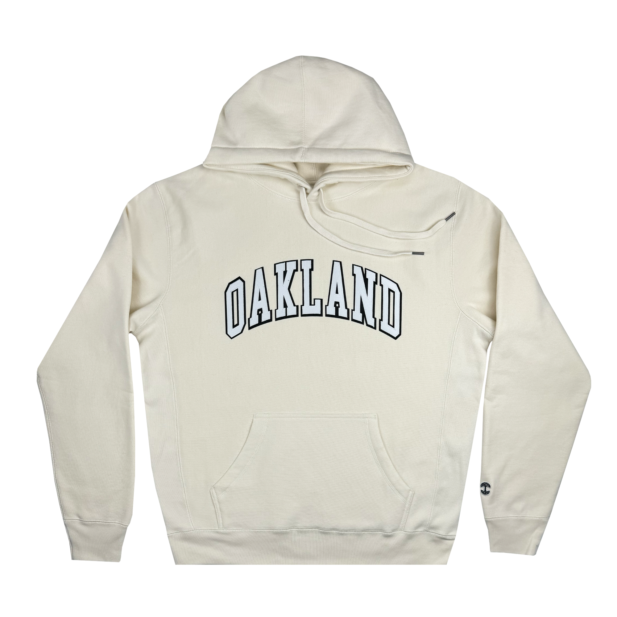 The Alma Mater Heavy Hoodie by Oaklandish is a cream-colored fleece pullover featuring "OAKLAND" in bold, black, arched letters across the chest. It includes a front pocket and a drawstring hood, with a small, stylized "C" logo on the lower left sleeve. The hoodie is displayed flat against a white background.