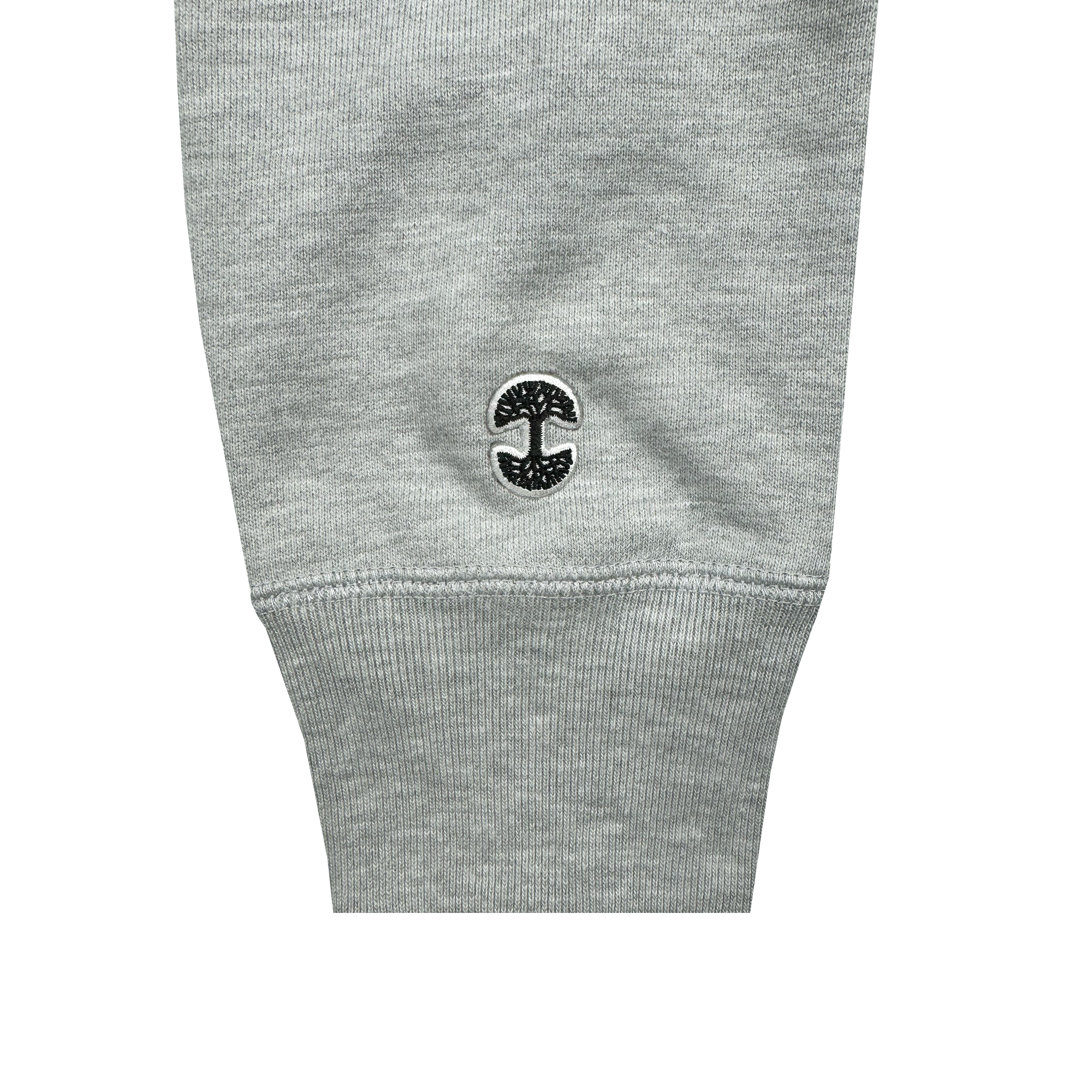 The sleeve of the Alma Mater Heavy Hoodie by Oaklandish is gray with a ribbed cuff. Near the cuff, you'll find a small, black embroidered logo featuring Oaklandish's stylized tree above an arch that looks like the letter "C." The fabric has a soft and slightly heathered texture, similar to heavyweight fleece in a classic pullover hoodie.