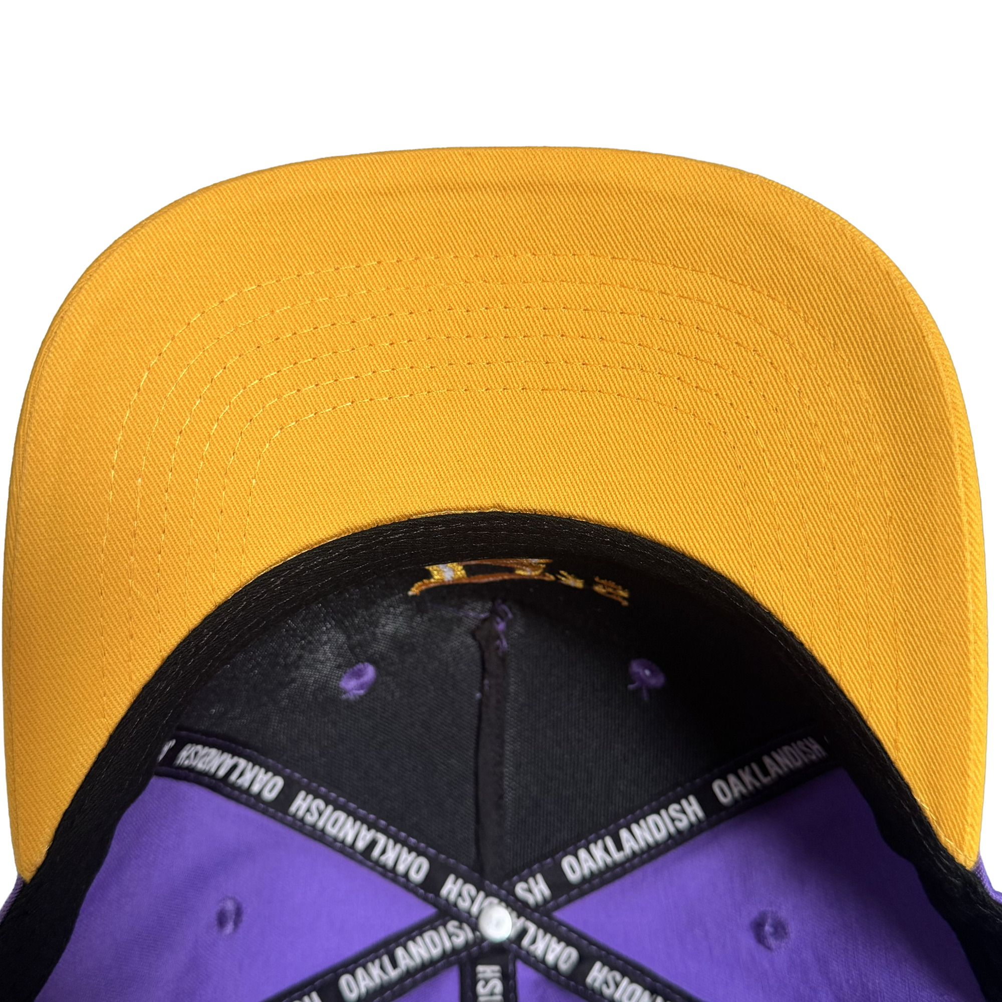 Overhead view of the Oakland Ballers 5 Panel Cap by Oakland Ballers, featuring a bright yellow bill, purple interior panels, black band, and “OAKLANDISH OAKLANDISH” text on the inner tape—a stylish nod to the proud spirit of Oakland baseball team fans.