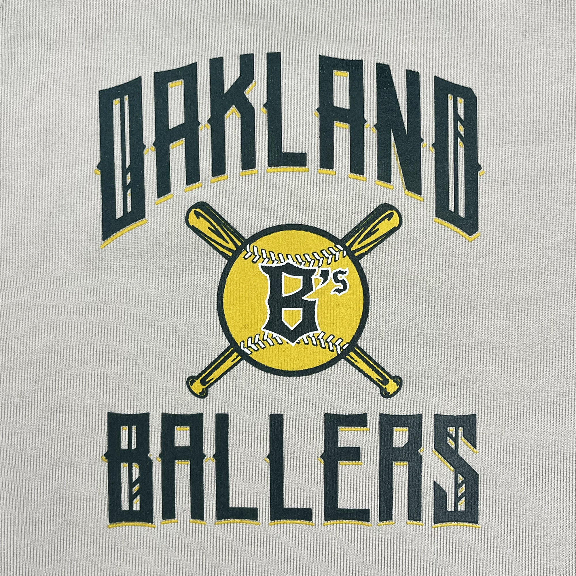 The image displays an Oakland Ballers Heavy Baseball Jersey featuring the text "OAKLAND BALLERS" in dark green and gold, styled in an arch at the top and bottom. At the center, there is a yellow baseball with "B's" written on it, accompanied by two crossed wooden bats behind the ball, symbolizing the professional baseball team from the Pioneer League.