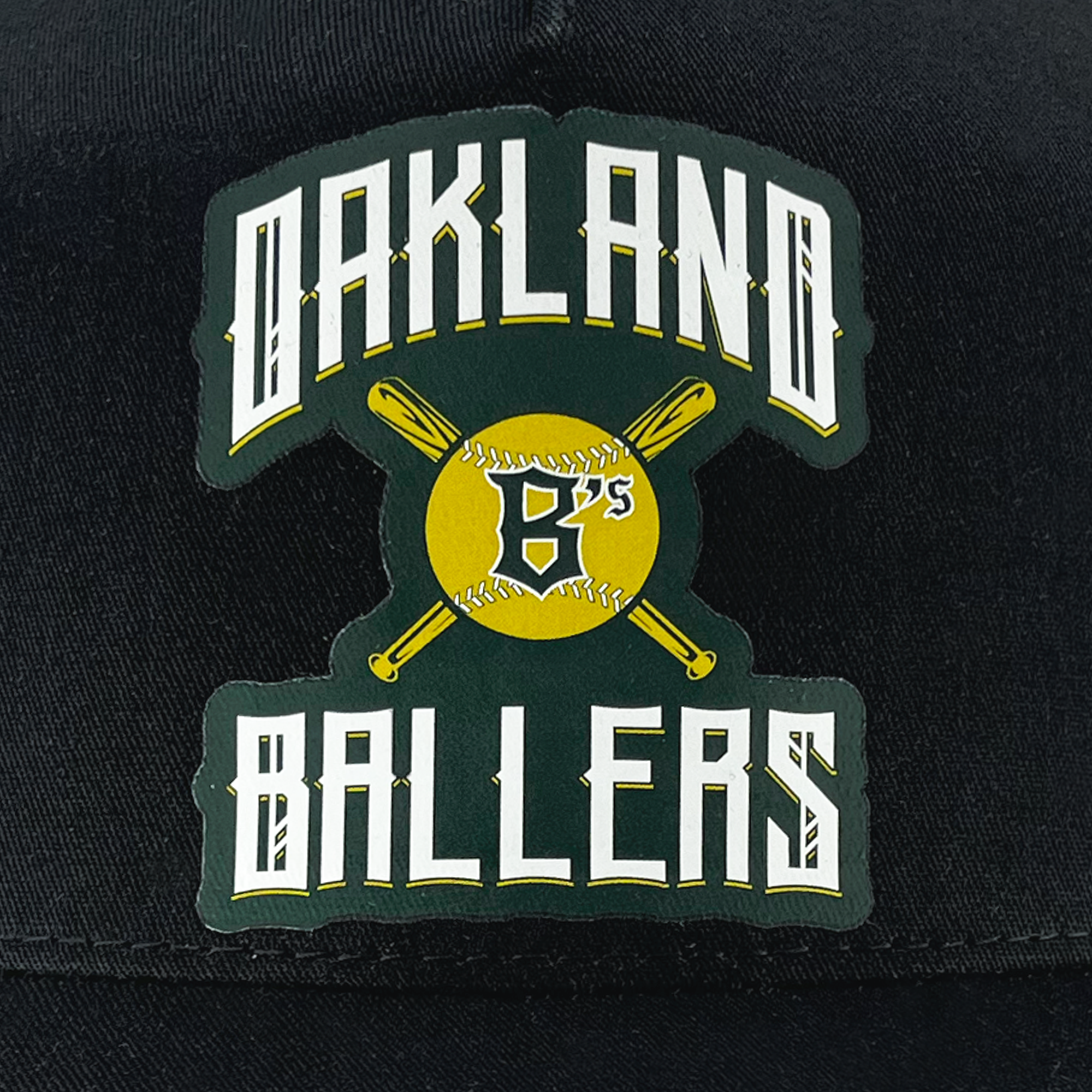 The Oakland Ballers Alt. Logo Curved Visor Trucker is a black cap featuring the Oakland Ballers logo at the front. The logo showcases "OAKLAND BALLERS" in a stylized white and yellow font, with a yellow baseball with two intersecting bats behind it and the letters "B's" in black on the baseball, celebrating their Pioneer League heritage.