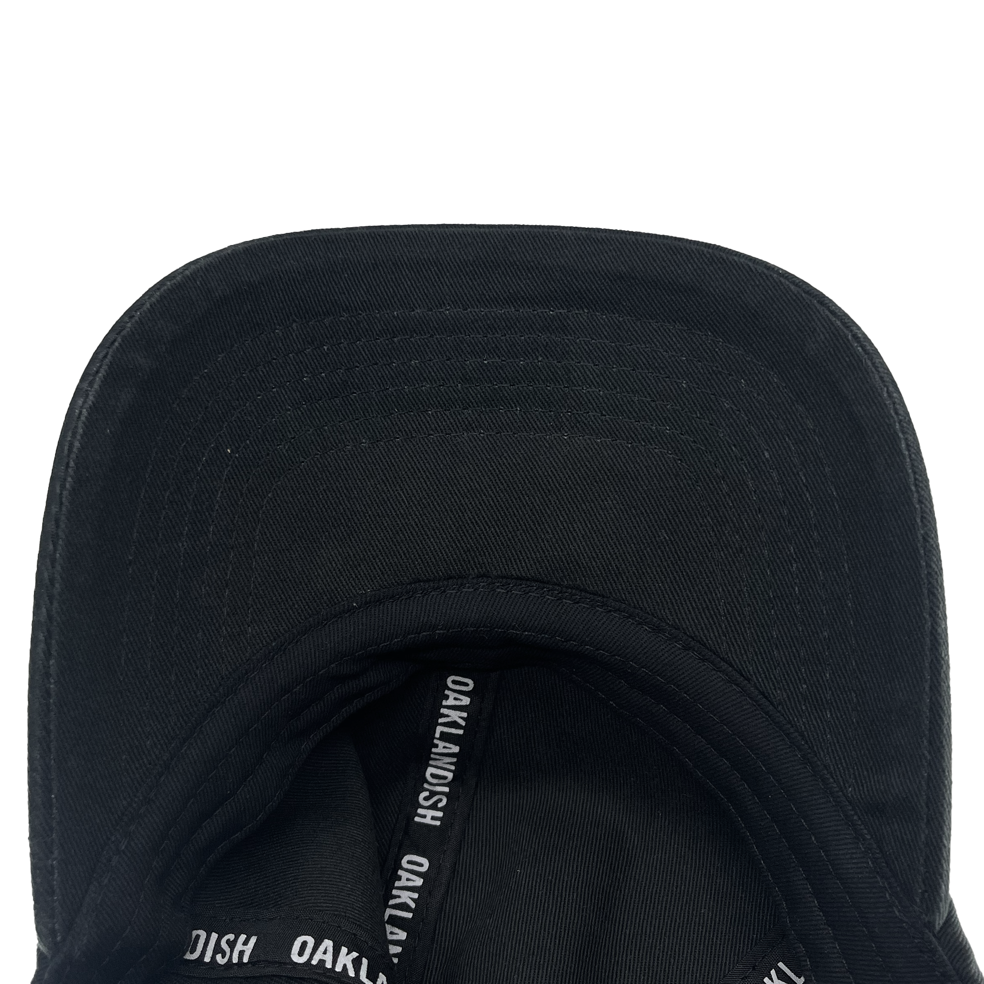 A close-up image of the interior from the front of an Oakland Ballers Dad Hat, showcasing the black ribbon inside label that repeatedly reads "OAKLANDISH." The brim's stitching is visible, and the slightly worn fabric gives it a casual, used look—ideal for any Oakland Ballers fan.