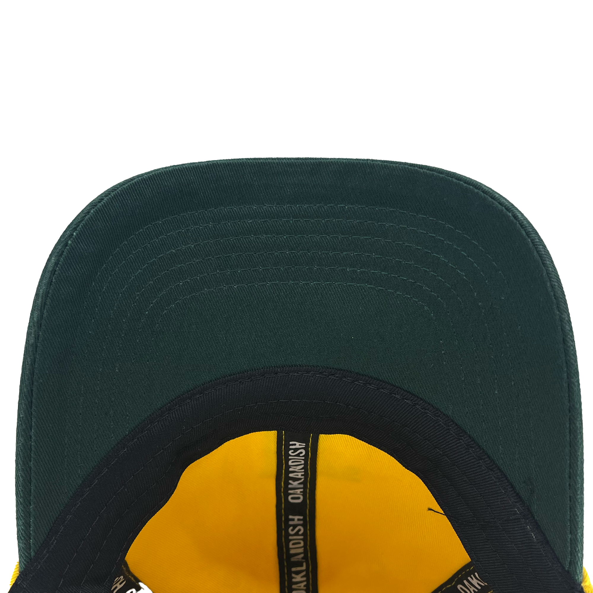 An overhead view of the underside of the Oakland Ballers Dad Hat reveals a dark green baseball cap. The brim stands out, adorned with multiple stitched lines. Inside, there is yellow fabric and a black band featuring the repeated text "OAKMOSH," representing Oakland Ballers from the Pioneer League.