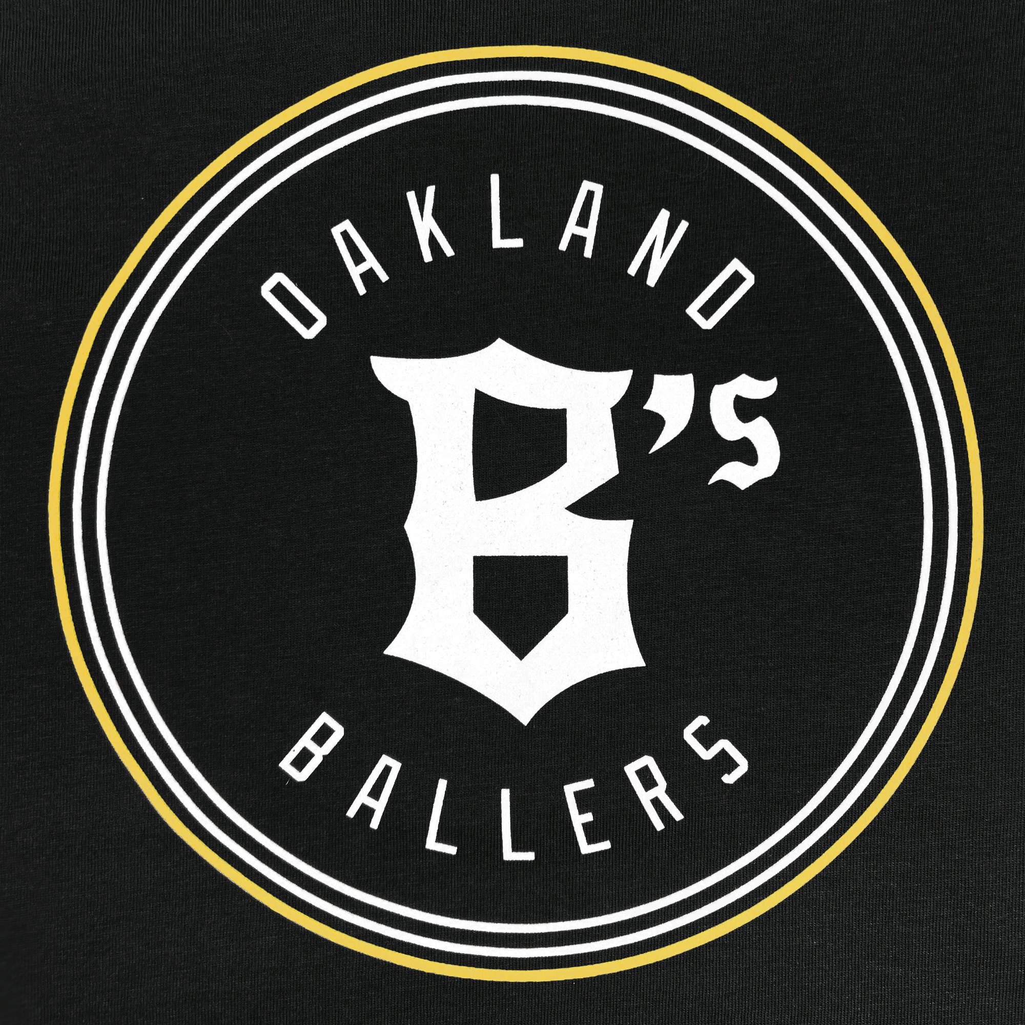 The Youth Oakland Ballers Logo Hoodie by Oakland Ballers features a circular logo on a black background with a white and gold border. Bold white text reading "Oakland Ballers" curves along the top and bottom of the circle. The center showcases a large, stylized "B," distinguished by its sharp and flowing design elements, symbolizing the Pioneer League professional baseball team.