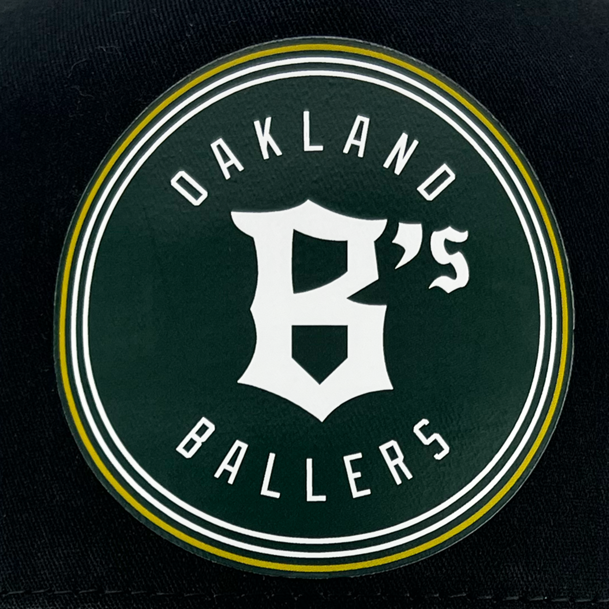 Featuring a circular logo with a black background and double white outline, the Oakland Ballers Classic Curved Visor Trucker showcases "Oakland Ballers" in bold white capital letters within the circle. The design includes large, stylized "B's" at its center, capturing a bold and sporty aesthetic that represents the Oakland baseball team in the Pioneer League.