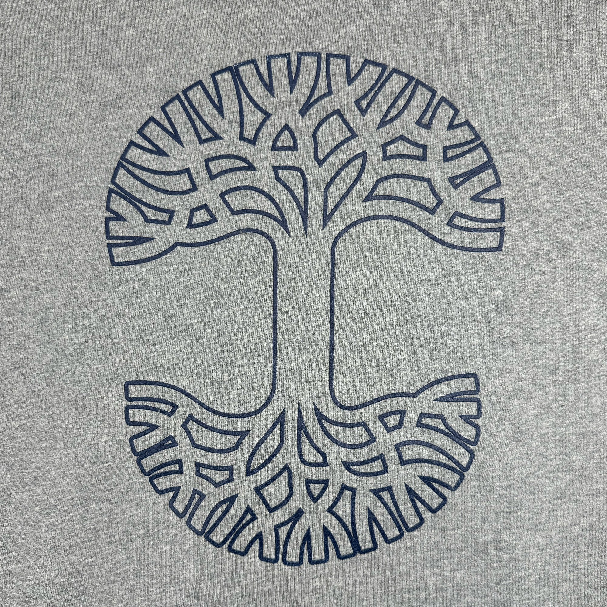 A heather grey Bandit Hoodie from Oaklandish features a stylized tree of life design. The navy blue tree, with intricately interwoven branches and roots, creates a symmetrical and circular pattern. This modern and artistic look stands out against the plain background, designed to provide a perfect fit in men's sizing.