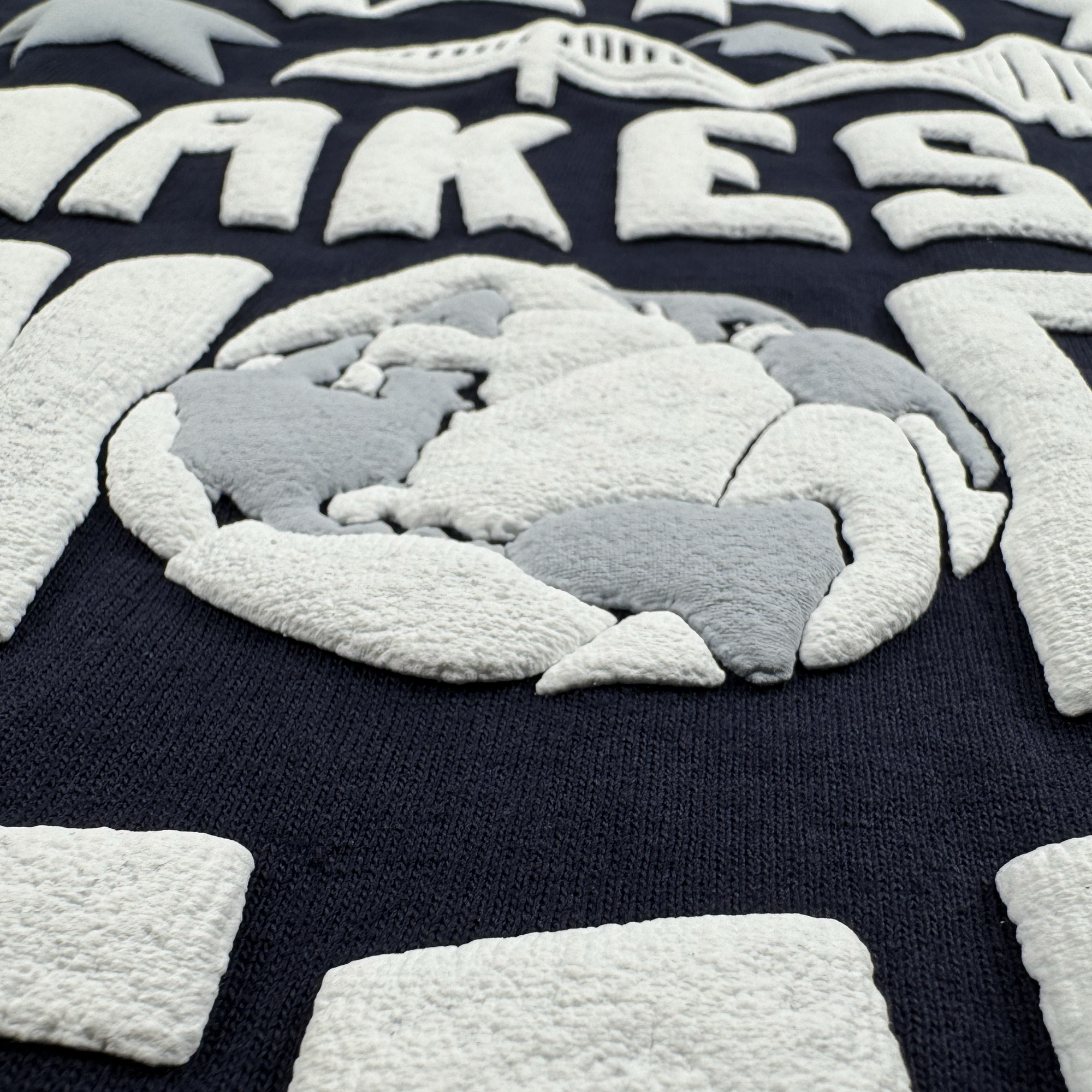 The Bay Bridge Tee by Oaklandish features a textured fabric design with white and gray abstract shapes on a dark blue background, including a central circular element, embodying global culture vibrancy and artful design.