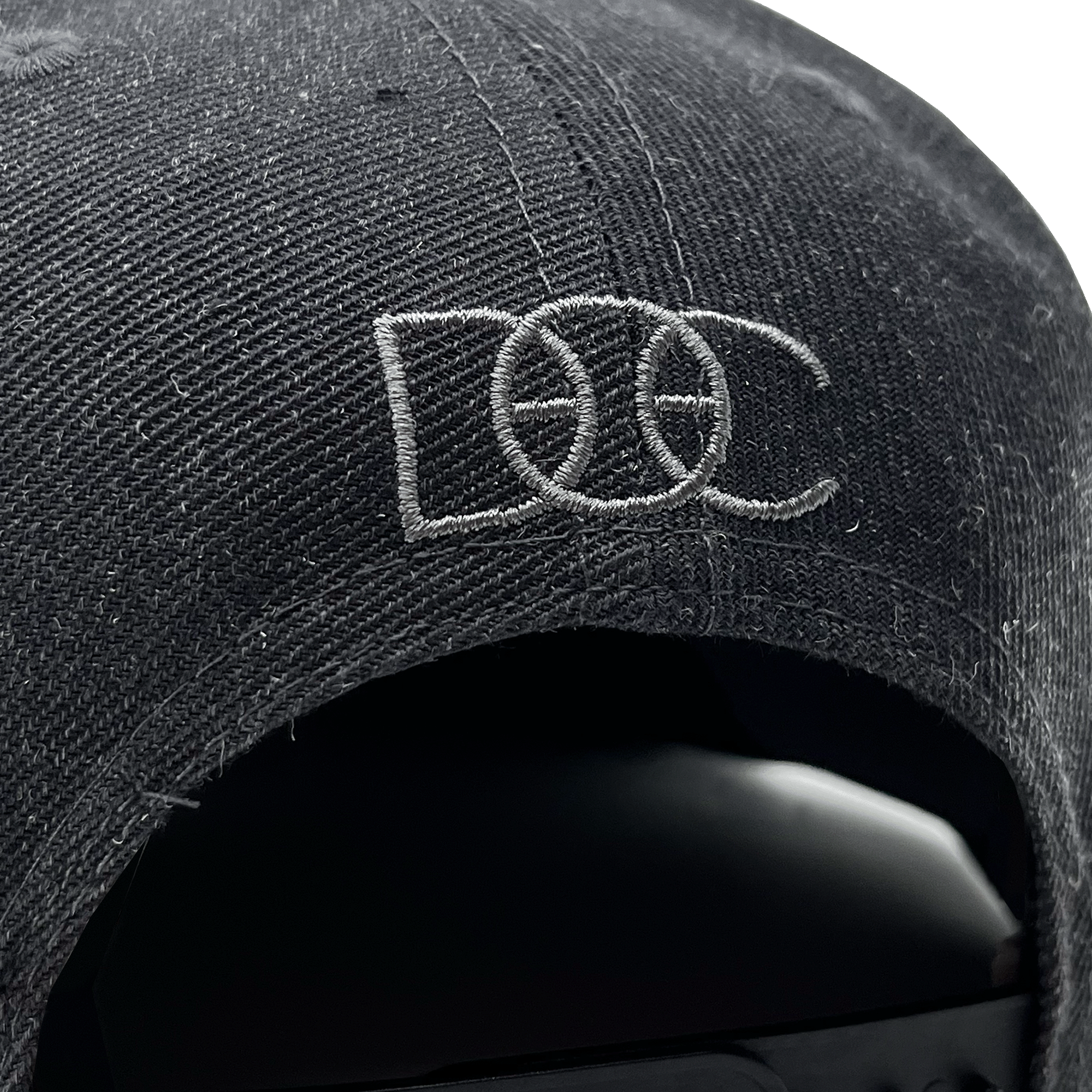 Close-up of grey embroidered overlapping DOC wordmark on the back of a charcoal hat.