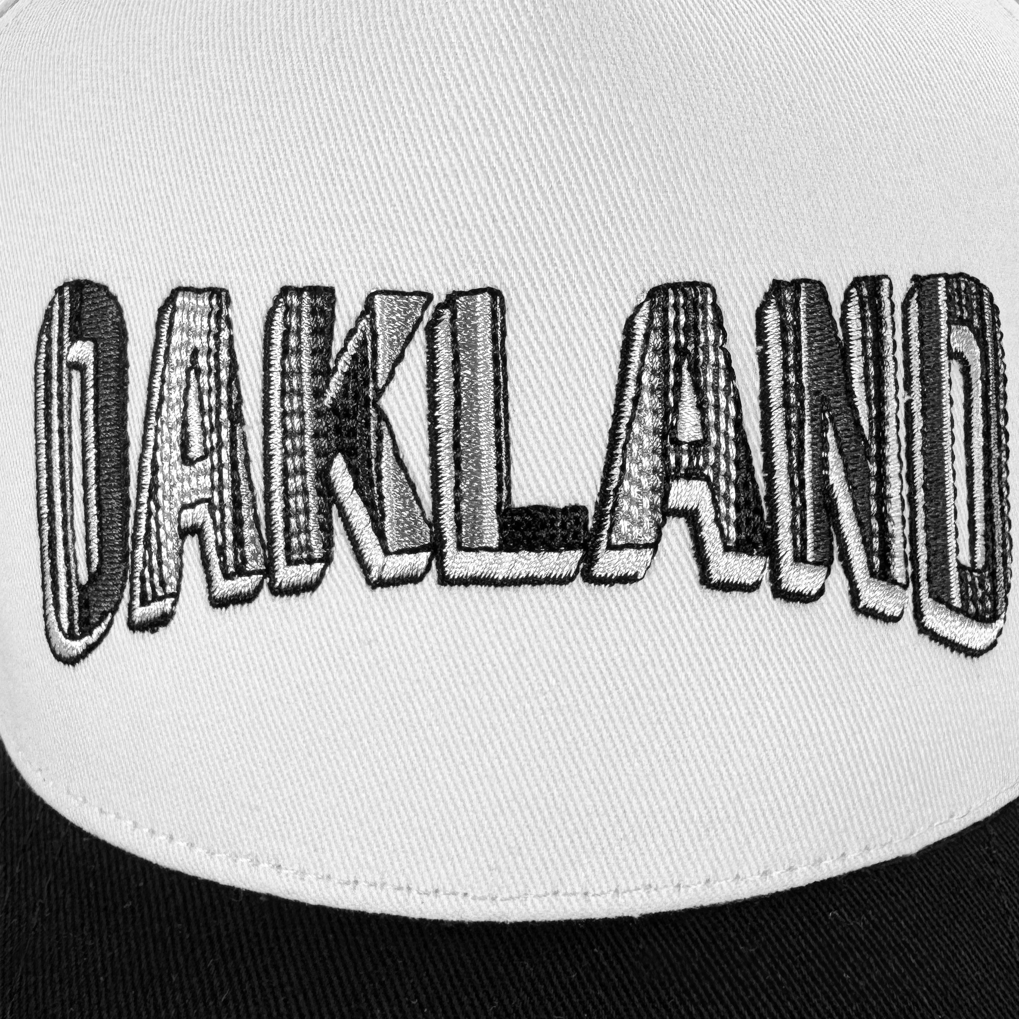 Close-up of the Oakland Ballers Oakland Beisbol 5 Panel Cap—a white snapback with bold, black and white embroidered "OAKLAND" text and a textured, three-dimensional look. Features a black brim inspired by classic Oakland Ballers style.