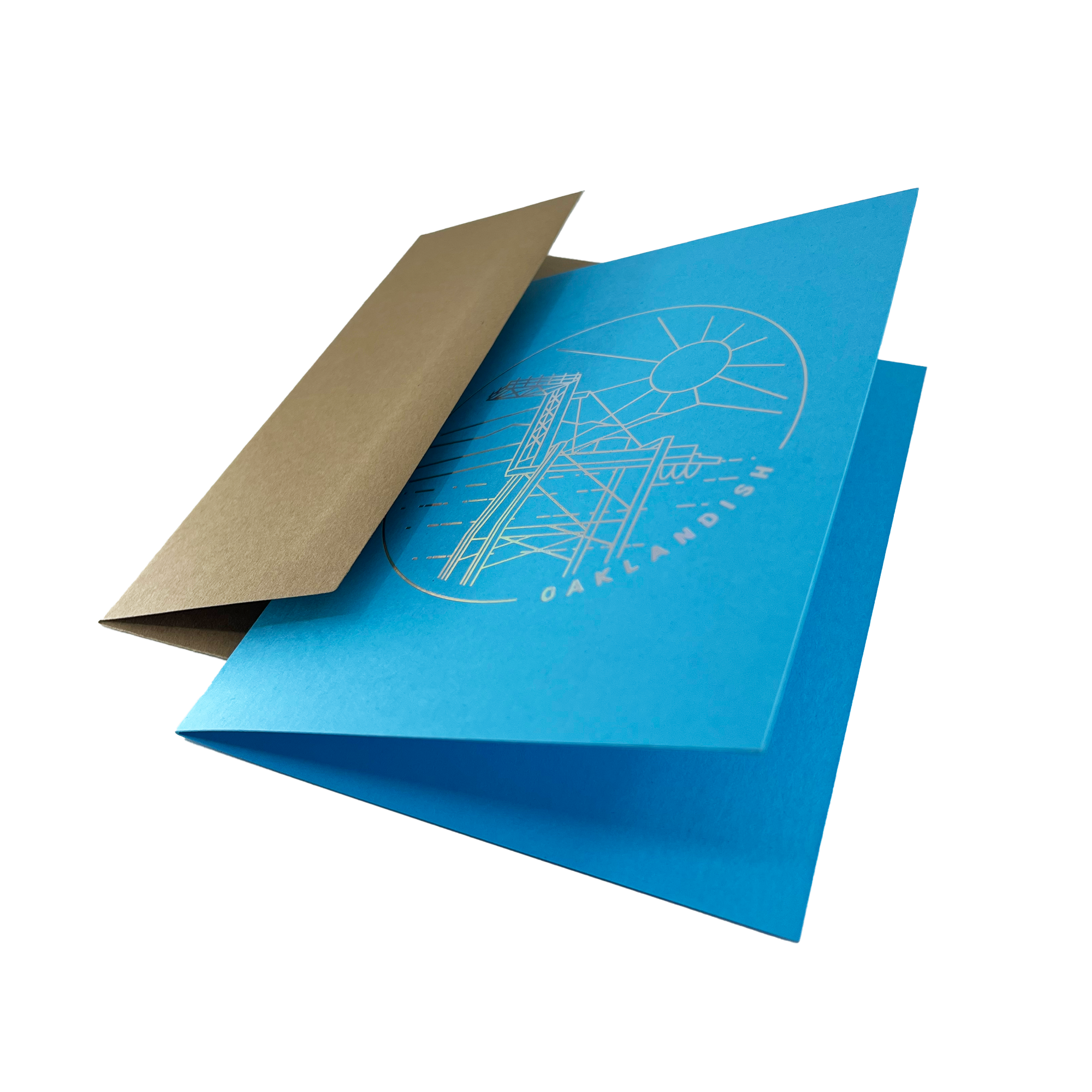 Open blue greeting card with a circular gold line drawing of an Oakland crane and OAKLANDISH wordmark with a brown envelope.