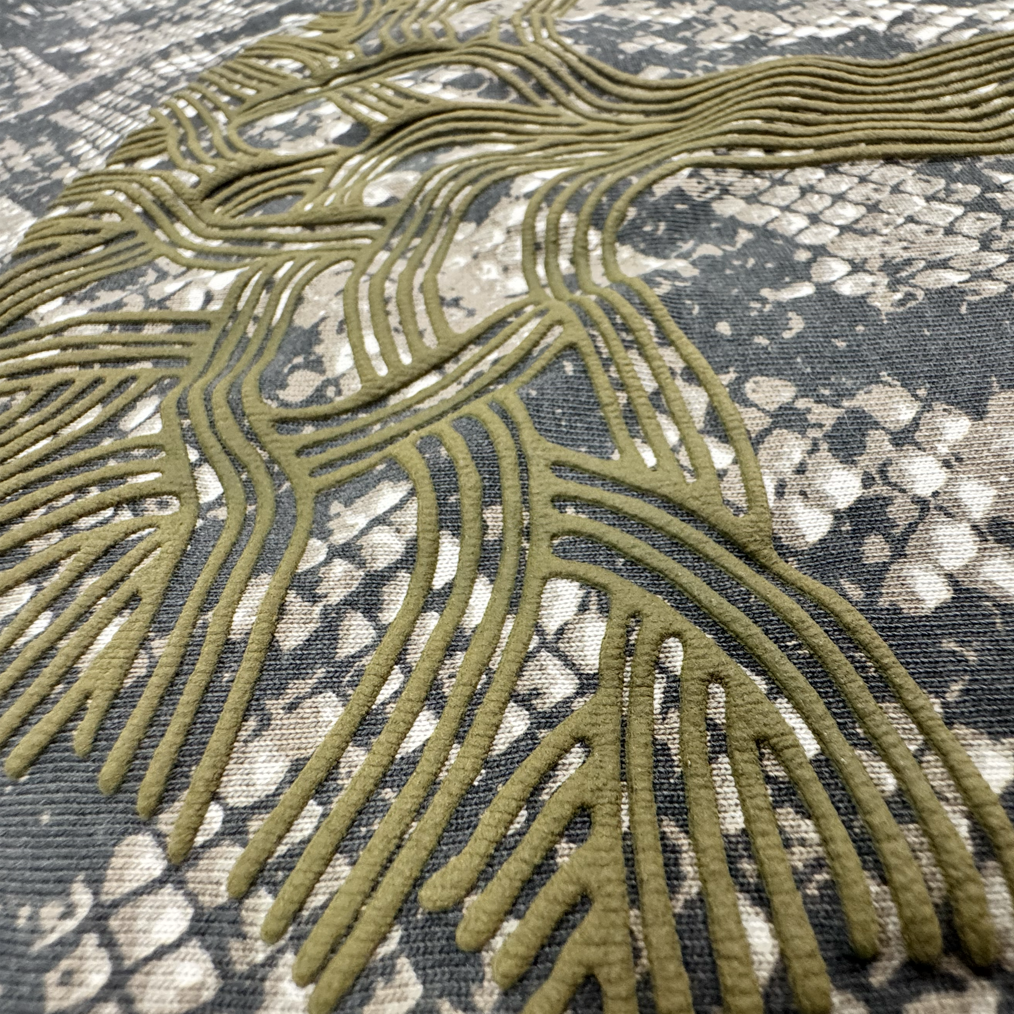 A close-up of fabric from the Oaklandish Classic Logo LS Tee by Oaklandish, featuring a textured, olive-green raised pattern reminiscent of flowing lines. The background showcases a mottled, snakeskin-like effect in grey and beige tones, providing striking contrast with the smooth linear design above it and the vintage black long sleeves that frame the look.
