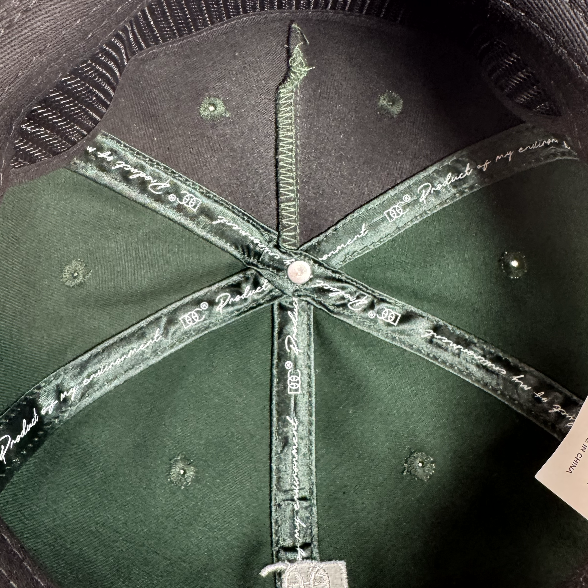 Close-up of the inside of the dark green Bay Area 5 Panel By DOC hat by Oaklandish, showing detailed stitching, seams, sweatband, green X-shaped band with white cursive writing, and a partially visible white tag.
