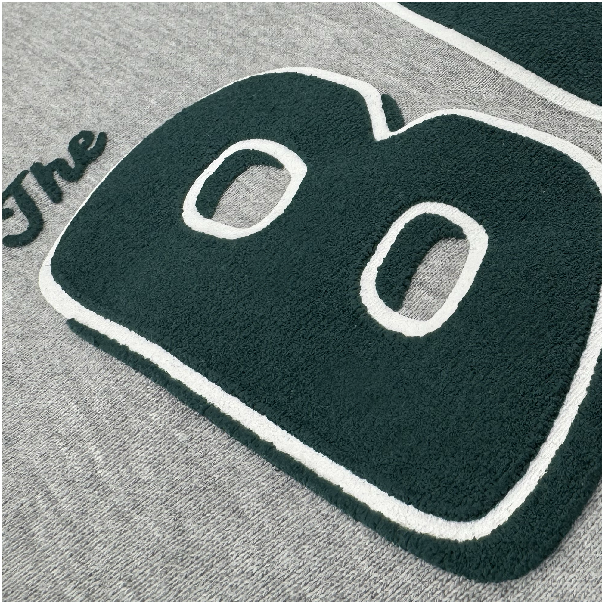 A close-up of gray heavyweight fleece on the Bay Area CC Hoodie By DOC by Oaklandish, featuring bold, textured green and white embroidery spelling "The B"—"The" in cursive and a larger "B"—in men's sizing.