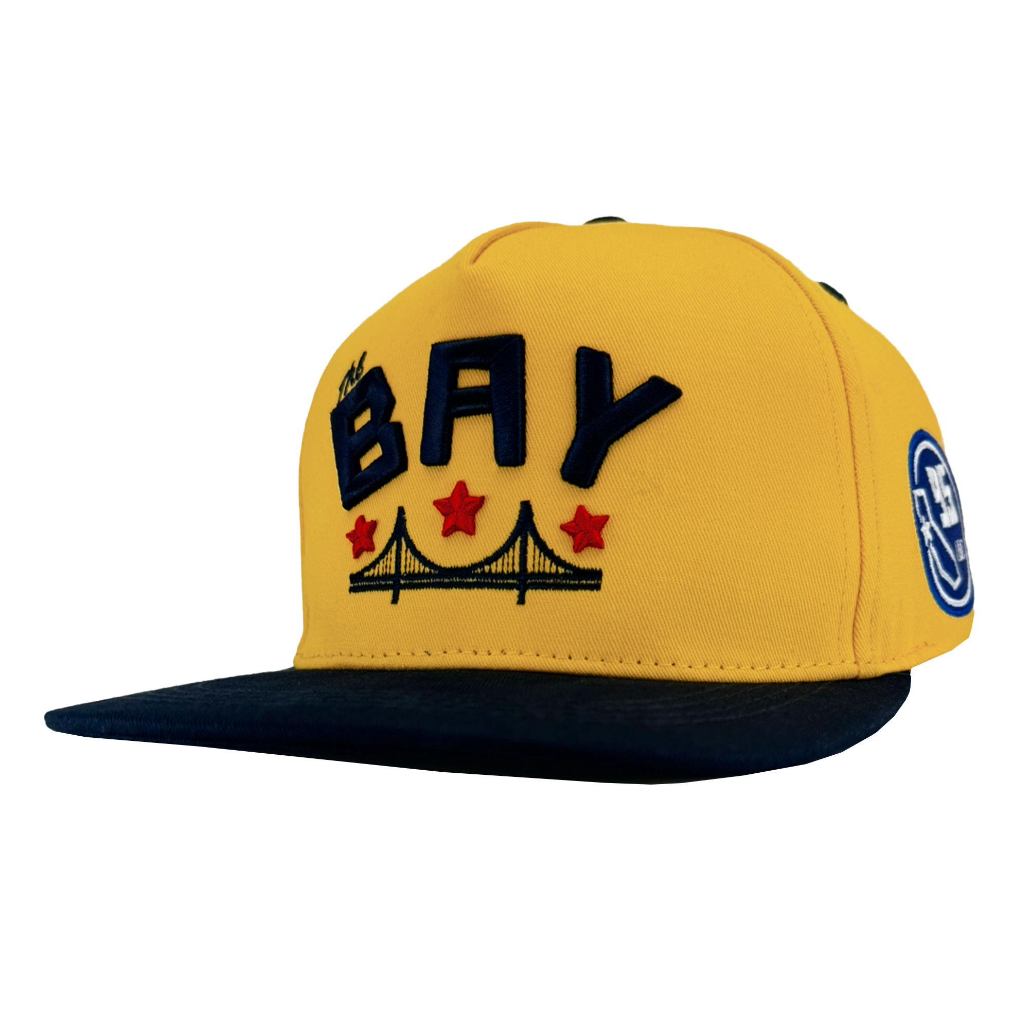 The Bay Bridge Snapback by DOC from Oaklandish is a yellow cap with a dark brim, featuring "BAY" in bold navy letters inspired by Bay Area art and design, a bridge illustration underneath, three red stars above it, and a circular DOC Snapback hat patch on the side.